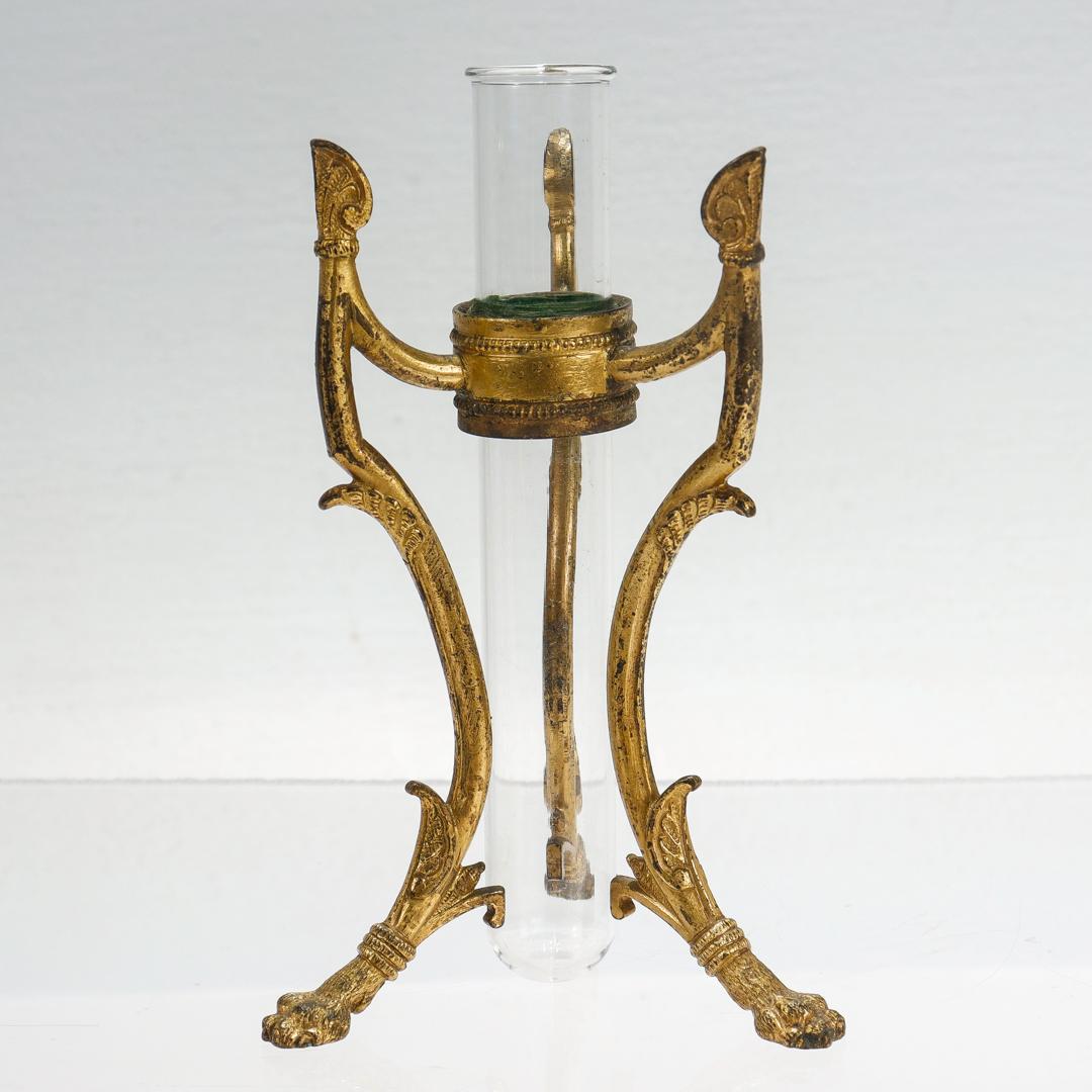 Vase à bourgeons de style néo-égyptien anglais.

En bronze doré (vermeil) et en verre.

Par A.I.C. Osler. 

Pieds à pattes poilues de style néo-égyptien et vase en verre en forme d'éprouvette reposant sur un anneau soutenu par trois