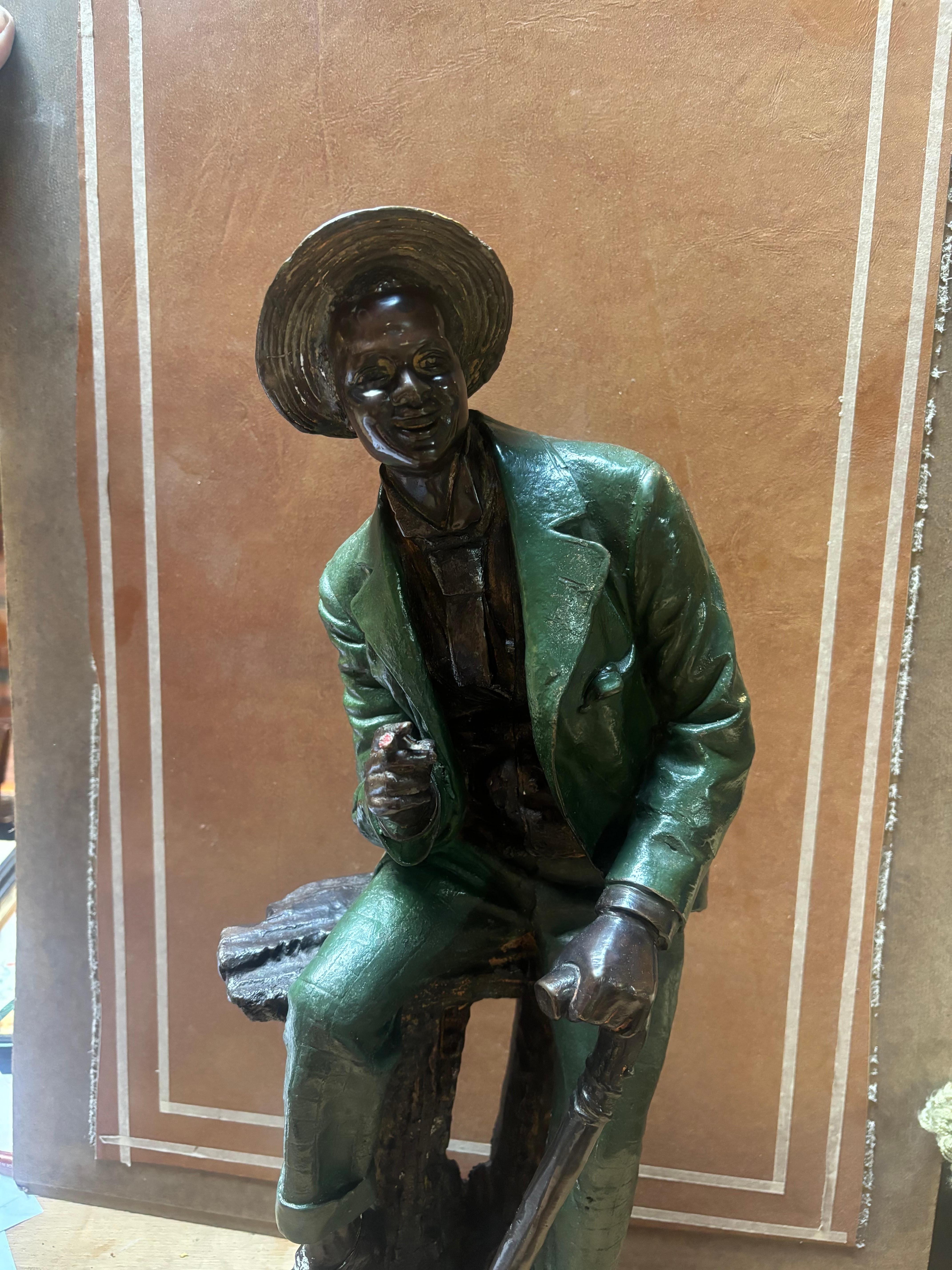 Grande scultura in bronzo di un gentiluomo meridionale con vernice originale. Questa scultura raffigura un uomo che fuma un sigaro seduto su un alto sgabello o una panchina con un bastone nell'altra mano. La vernice si è usurata nei punti di maggior