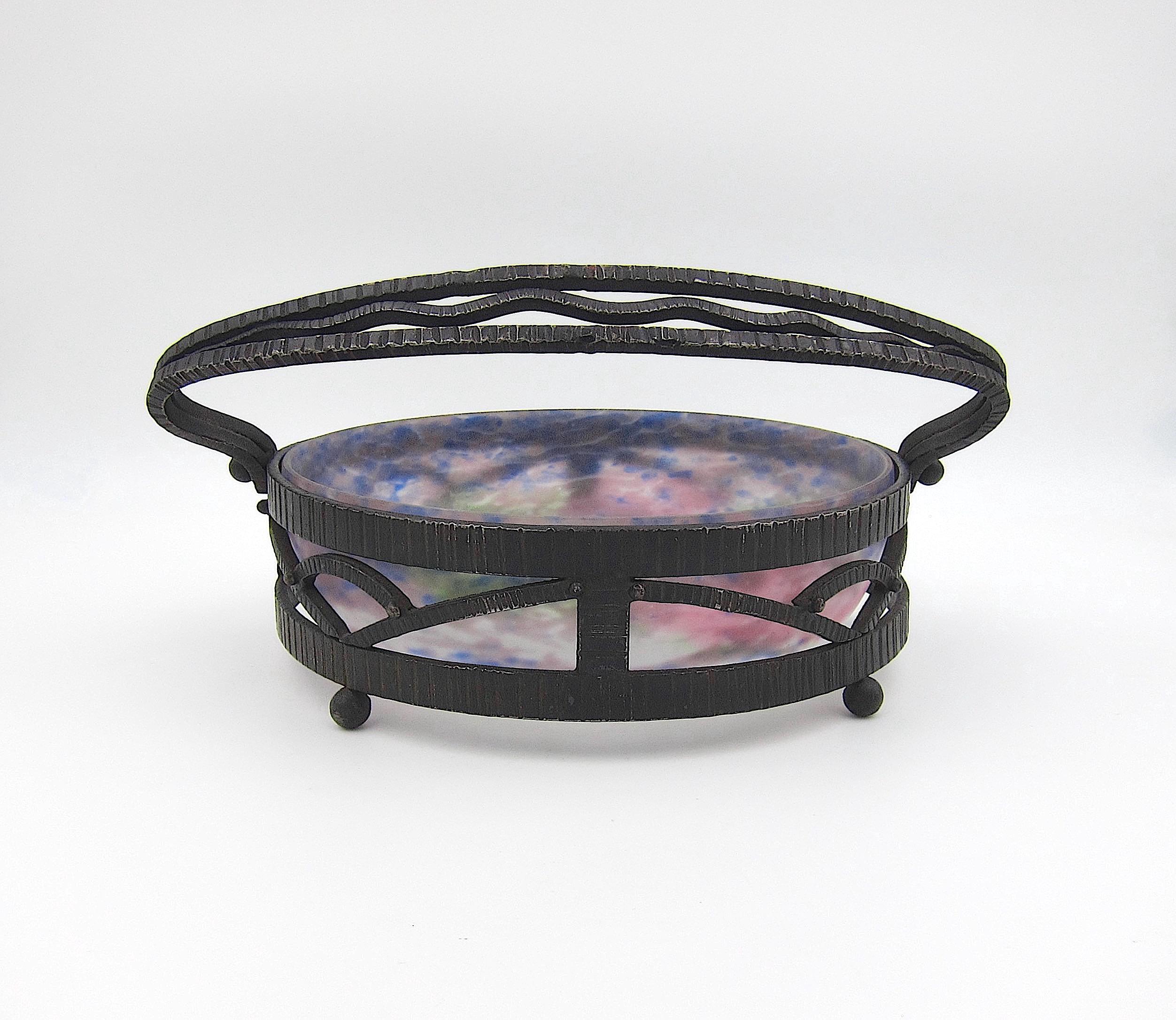 A French Muller Frères à Lunéville circular bowl fitted within a wrought iron carrier, dating circa 1920. The frosted art glass bowl with blue, green, and pink mottled accents bears an acid-etched Muller Fres / Luneville mark on the side. The