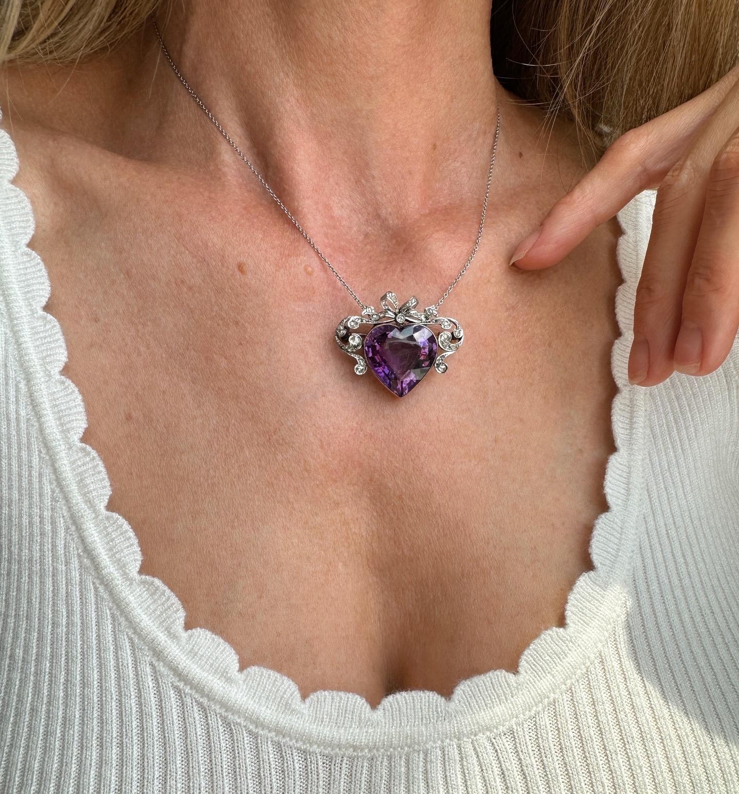 A romantic symbol of love from the turn of the 20th century, France. A regal and deeply saturated amethyst heart, bracketed by diamond lined scrolls and crowned with a glittering rose-cut diamond bow, is a visual reminder that love is a precious