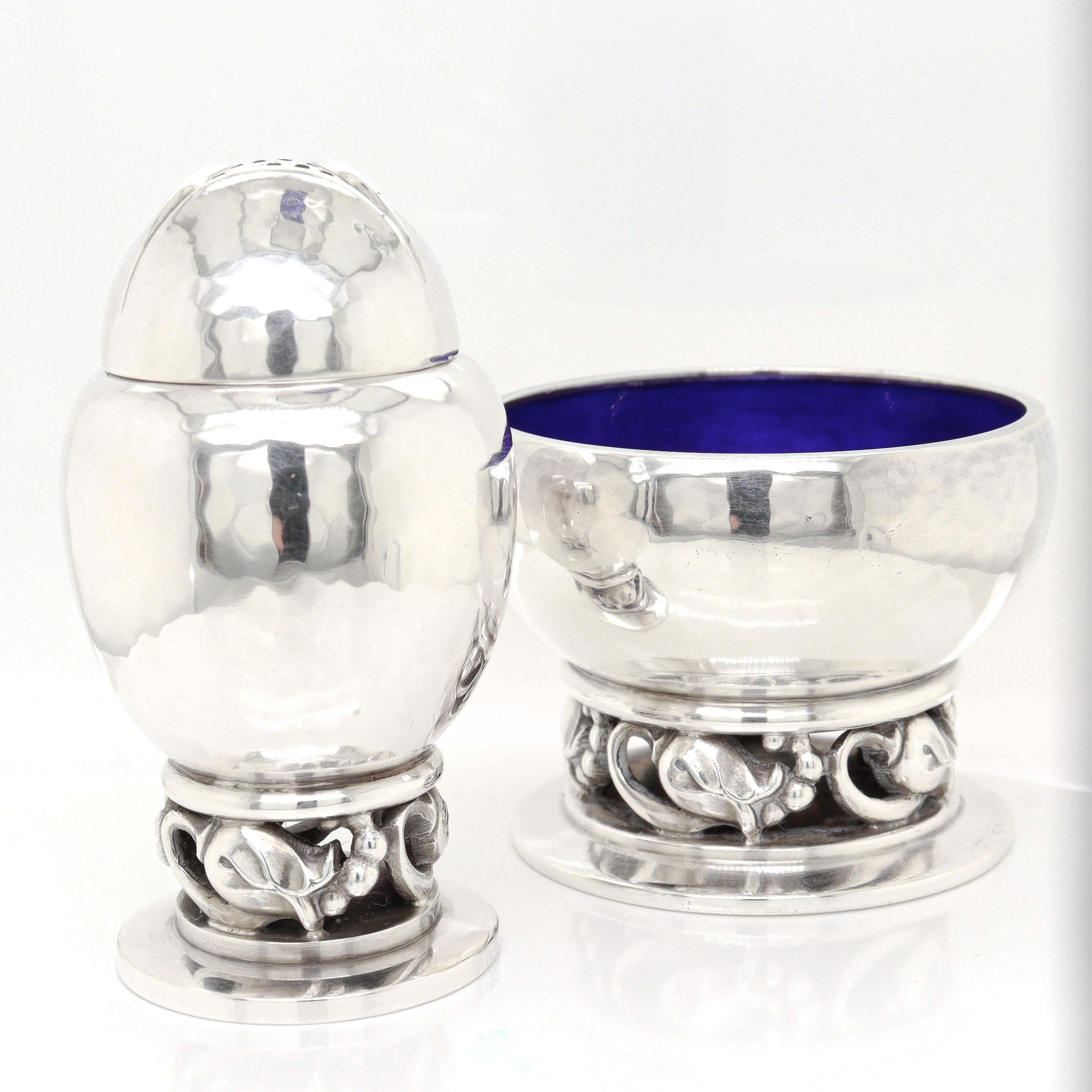 Una raffinata coppia di saliere e pepiere moderne danesi firmate.

Di Georg Jensen.

In argento sterling.

Modello a fiore n. 2A. 

Disegnato da Georg Jensen nel 1905 circa. 

Comprende una pepiera, una saliera aperta con una ciotola smaltata in blu