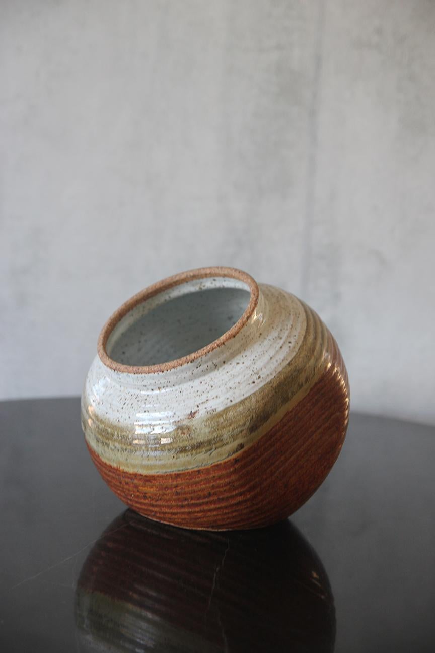 This signed earthenware vase, masterfully hand-thrown, showcases a distinctive design characterized by its unique shape and flat side. Its surface is adorned with a glossy glaze that beautifully blends shades of green, brown, and grey, creating an