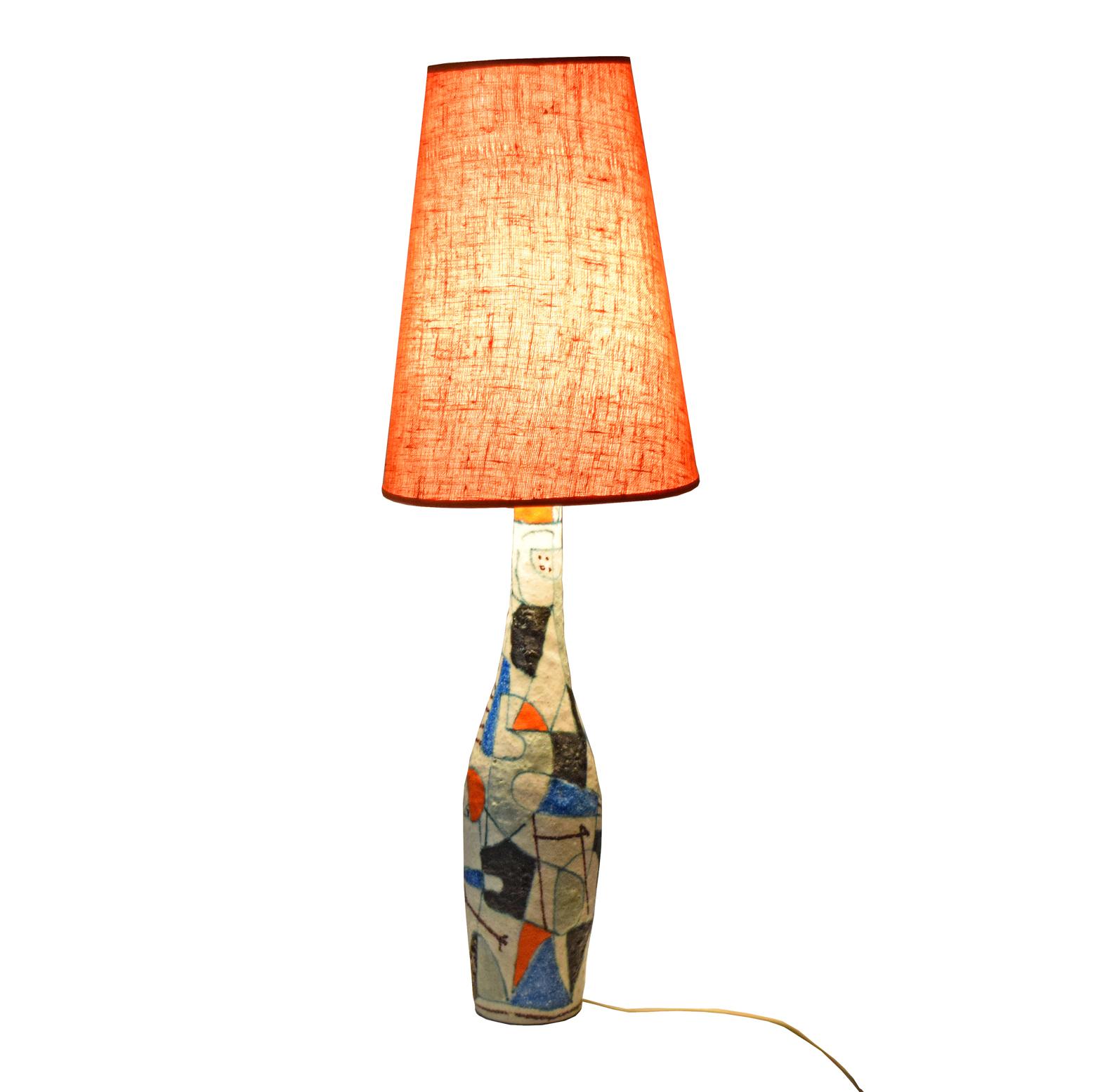 Tall, narrow faience table lamp. Decorated with blue, orange-red, Bordeaux-red, black, blue and green lava glaze in a graphic decor on a transparent base. Signed Gambone and with a “donkey”-mark. Including a conical shaped lampshade of white acrylic