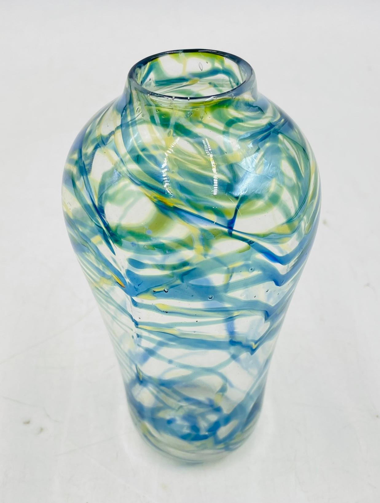 This hand-blown art glass vase is signed and dated 1975 by American glass artist Roland R. Correia. It features soft swirls of blue, green, and yellow over a clear glass base, creating a light and flowing look. The colors wrap around the vase in an