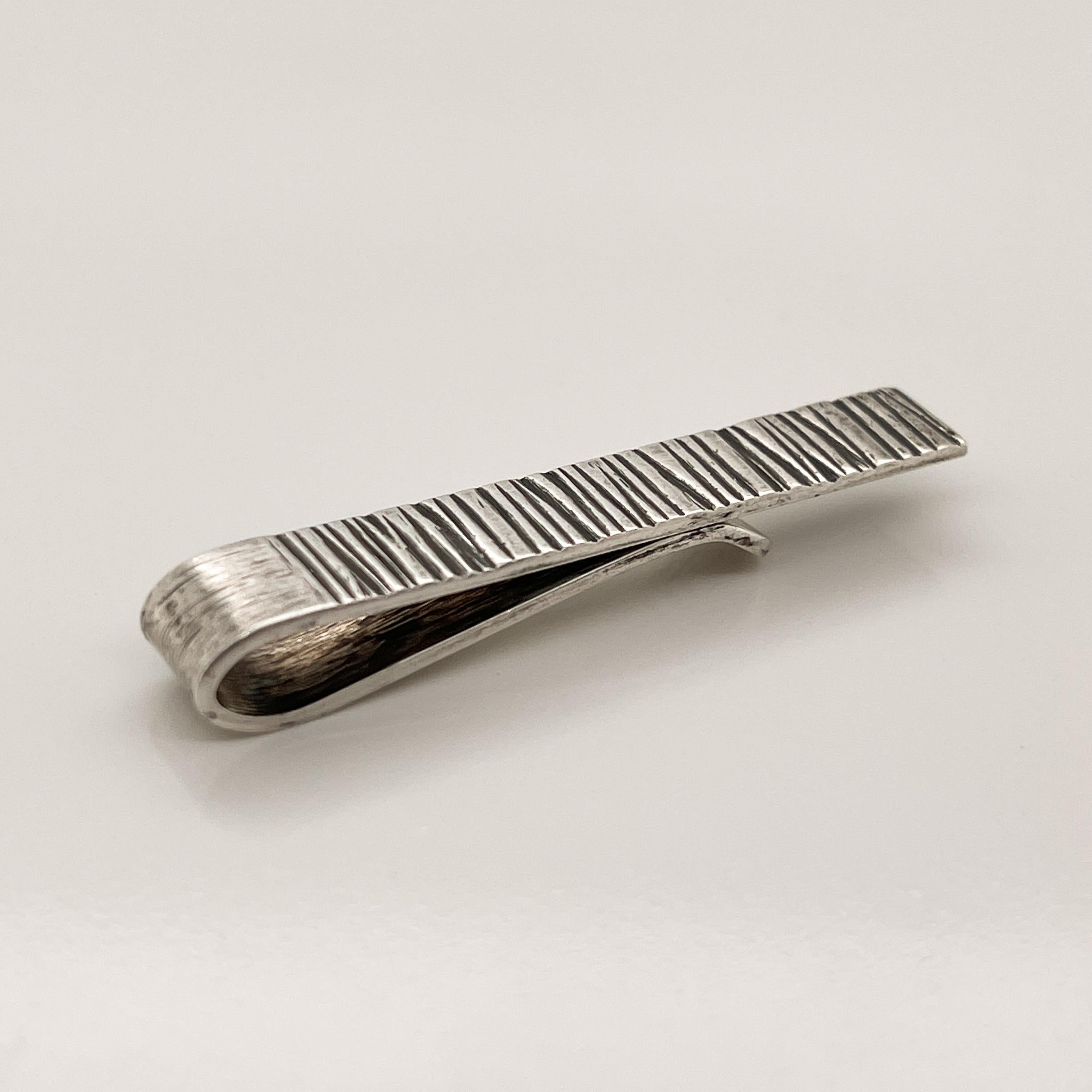 A fine Mid-Century tie bar or money clip.

By the California Modernist silversmith - Harold Fithian.

In sterling silver with an asymmetrically ribbed and brushed finished surface. The ribs recesses are liver sulfur patinated.

Simply a wonderful