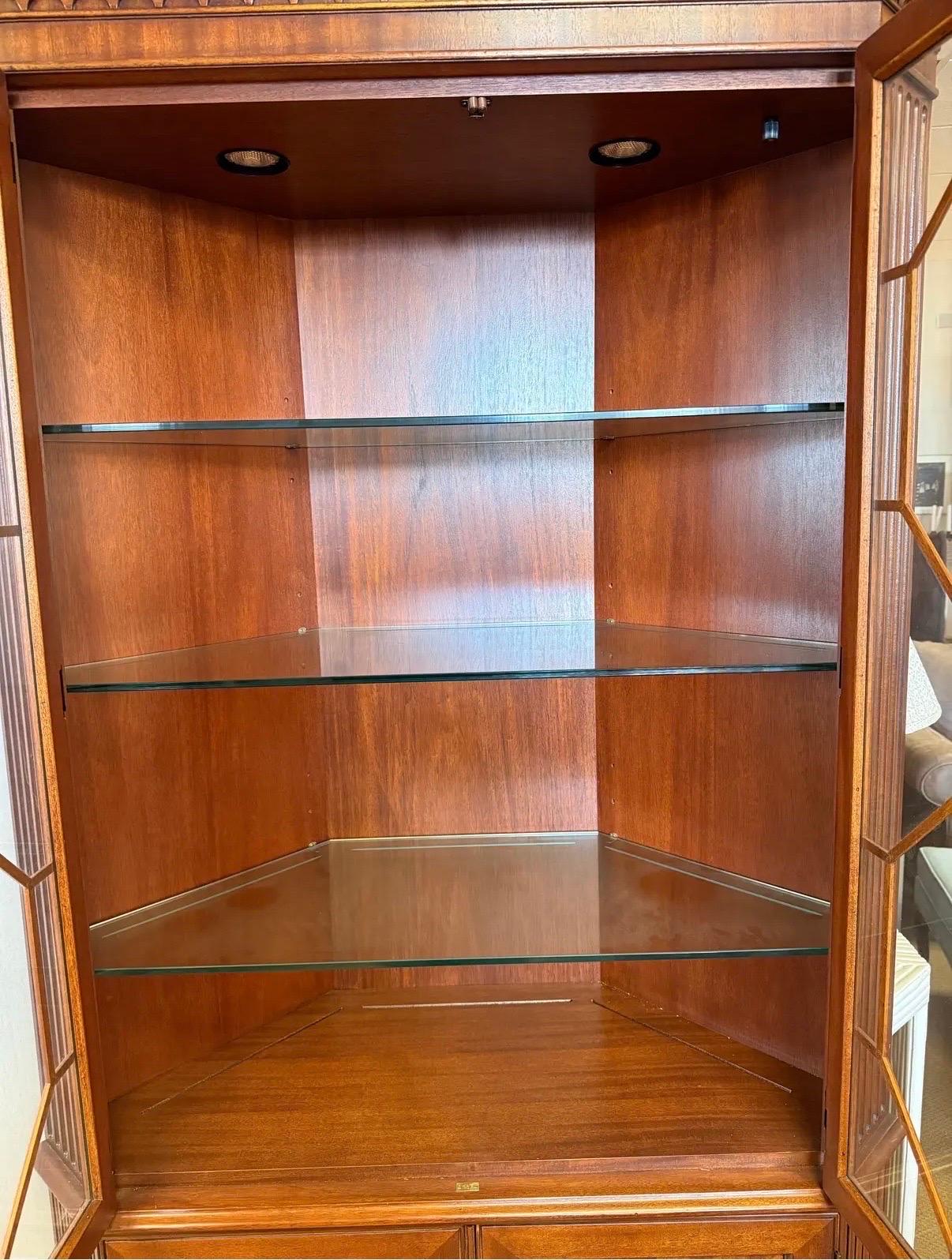 Exceptional hand carved Henredon mahogany corner cabinet that features well lit design with geometric symmetry and balanced detail as well as gorgeous lattice work front.  Glass shelves in side are illuminated up top and there is more storage down