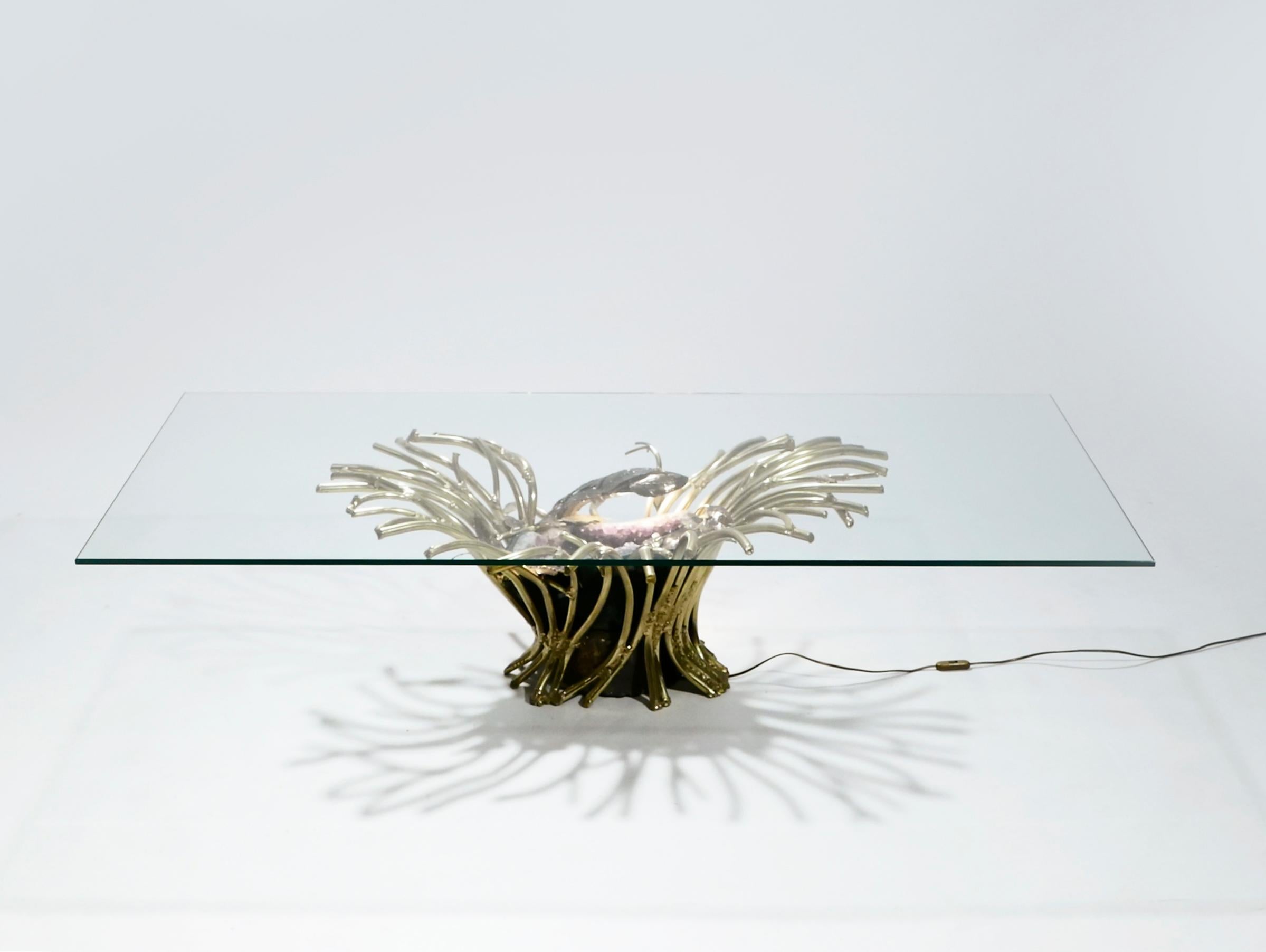 The creative design of this coffee table by Isabelle Faure is breathtaking. Tangled in a web of heavy brass “branches” is a monstrous amethyst geode, lit from the inside. This sculpture forms the base for a thick slab of transparent glass, a choice