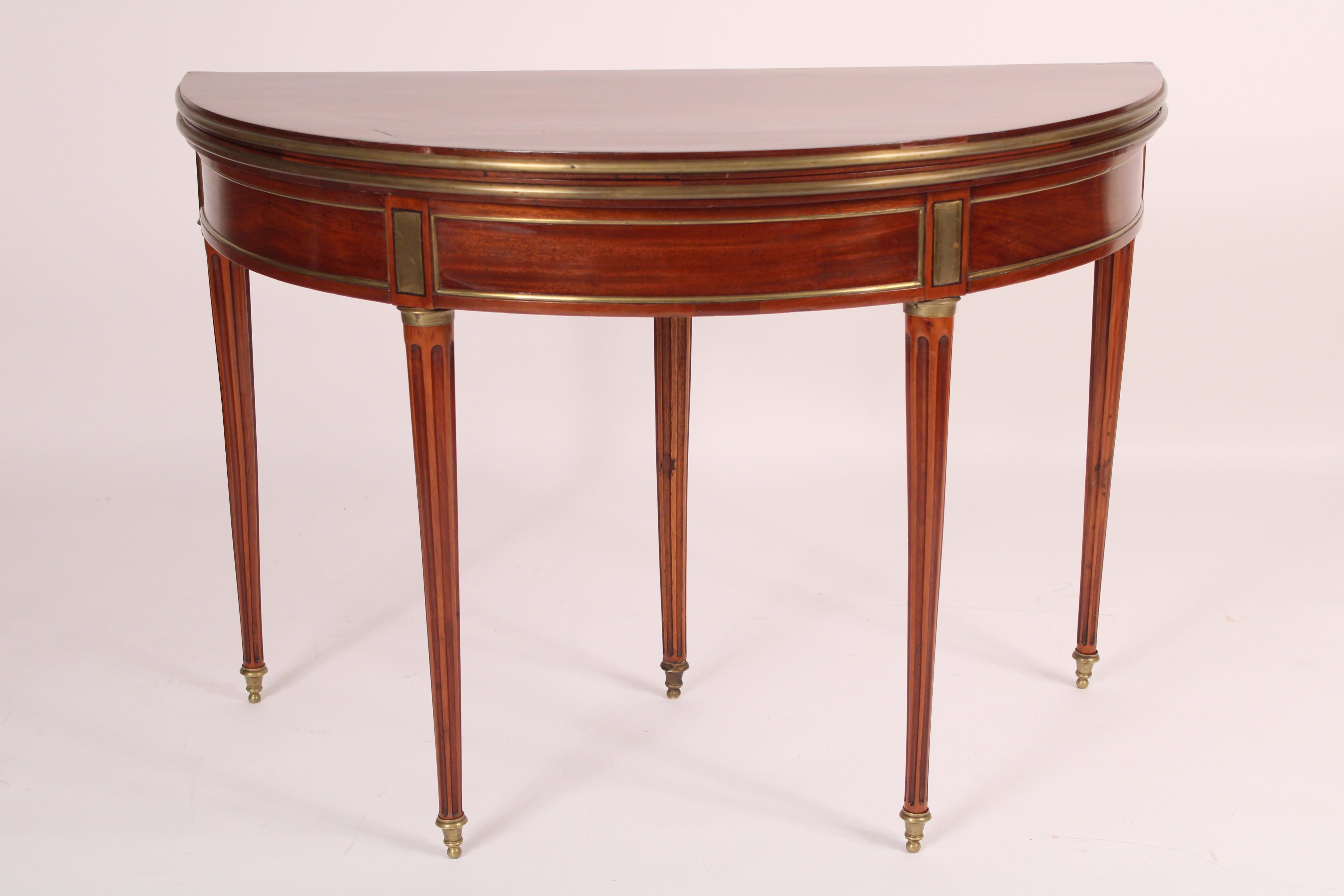 Antique Louis XVI style mahogany brass mounted demi lune games table, late 19th century, stamped Jansen. With a demi lune mahogany top with brass mounted edges, a demi lune frieze with 3 mahogany panels with brass frames, underside of frieze stamped