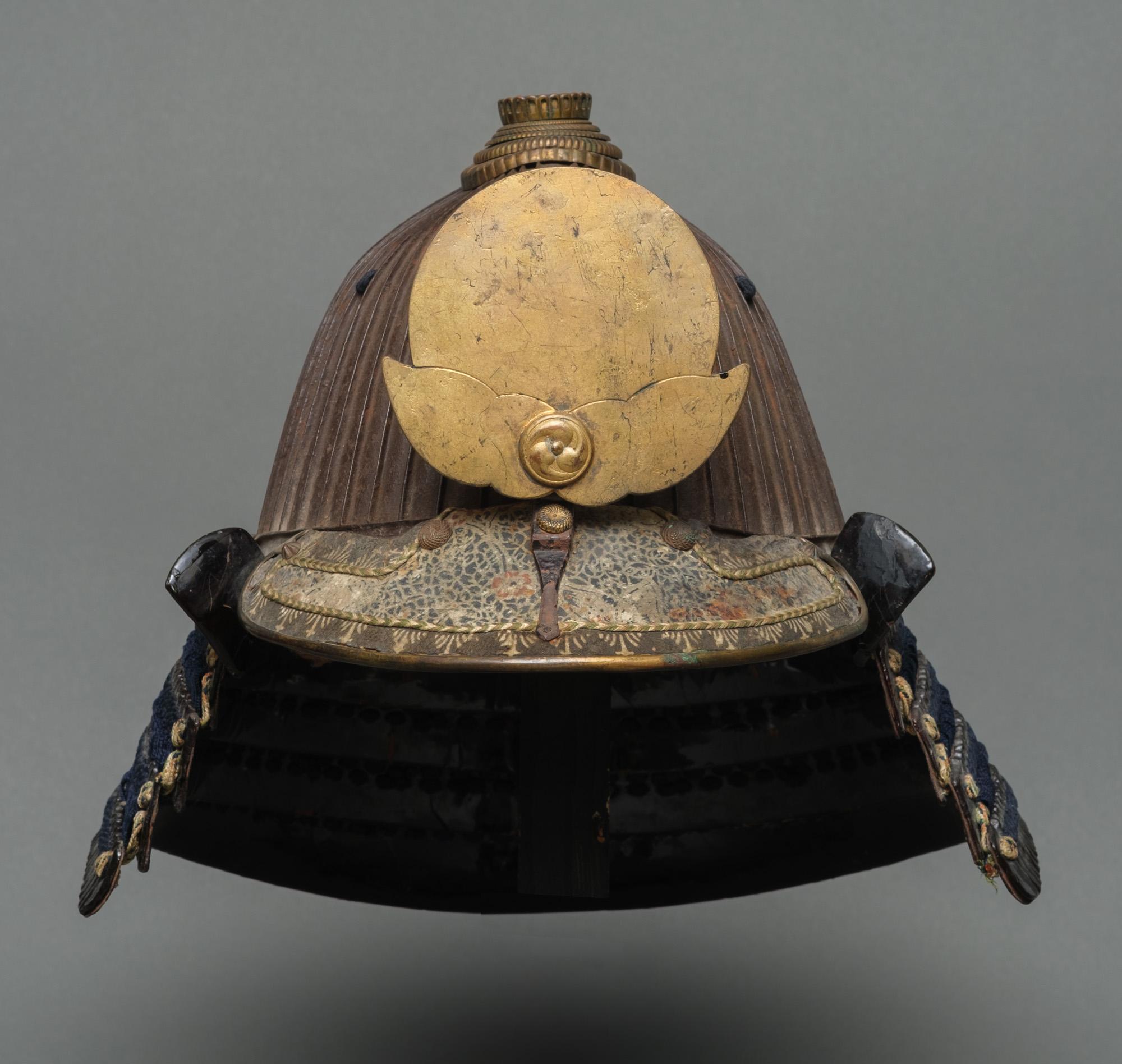 An antique, outstanding signed suji’bachi kabuto (helmet with ridges) surmounted by a gilt metal maedate (forecrest) shaped like a full moon emerging from the clouds heightened by a circular applique depicting three swirling commas