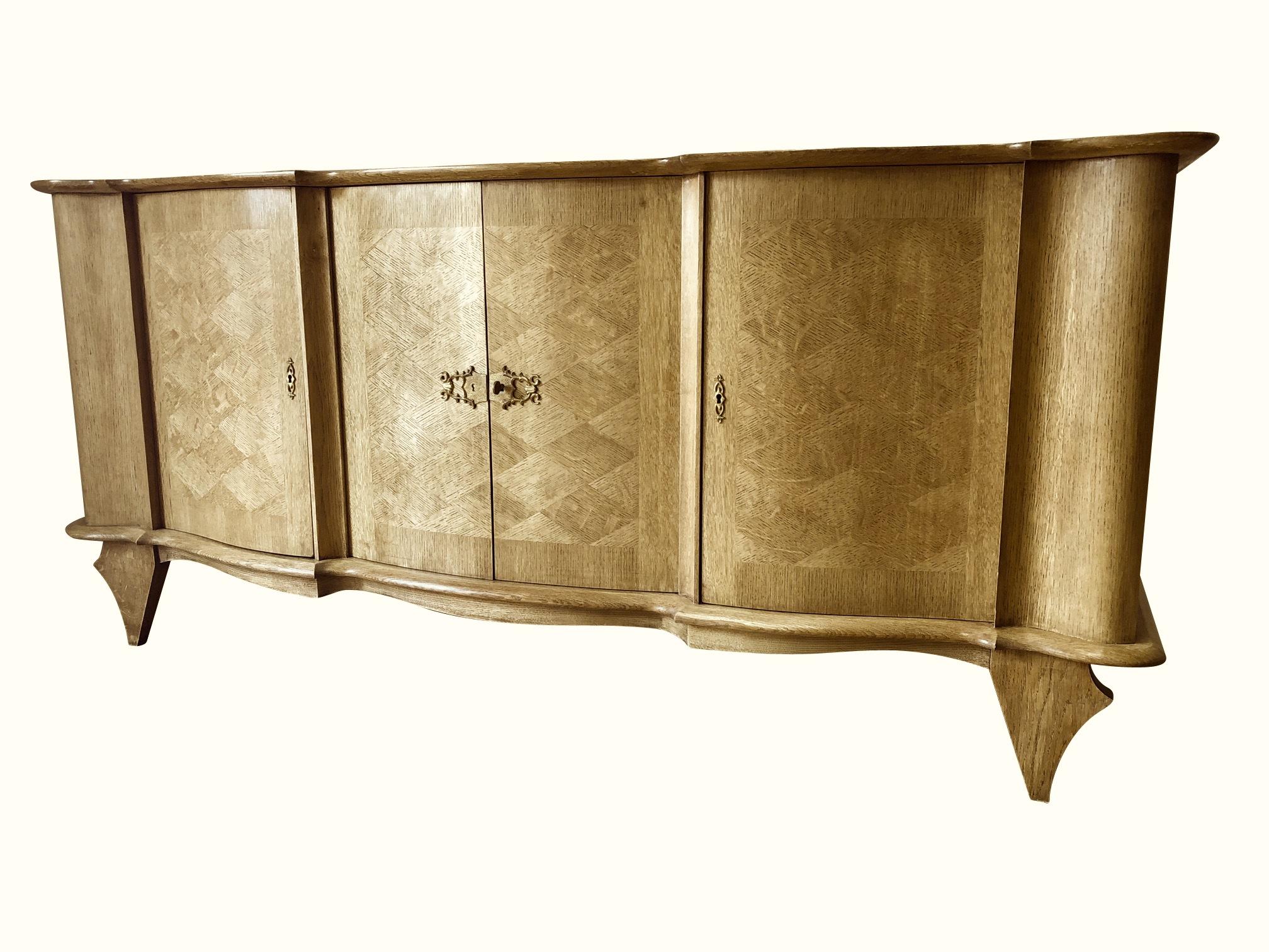 1940s French signed Jules Leleu oak credenza.
Diamond pattern parquetry veneer on doors and top.
Curved facade with four doors.
Sculptural legs.
Original ornate brass hardware.
Three interior shelves and two drawers.
 
