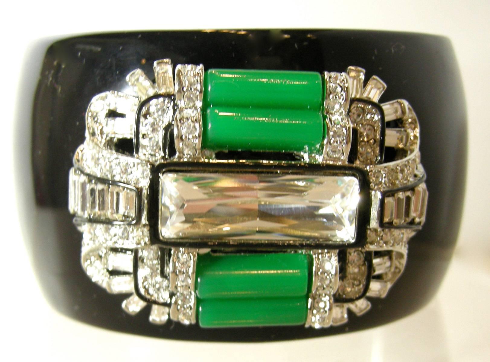 This Kenneth Jay Lane deco style clamper bracelet features faux jade rods with crystal accents on a black enameled setting. This clamper bracelet has spring-closure and it measures 6-3/4” x 1-3/4”.  It is signed “Kenneth Lane” and is in excellent