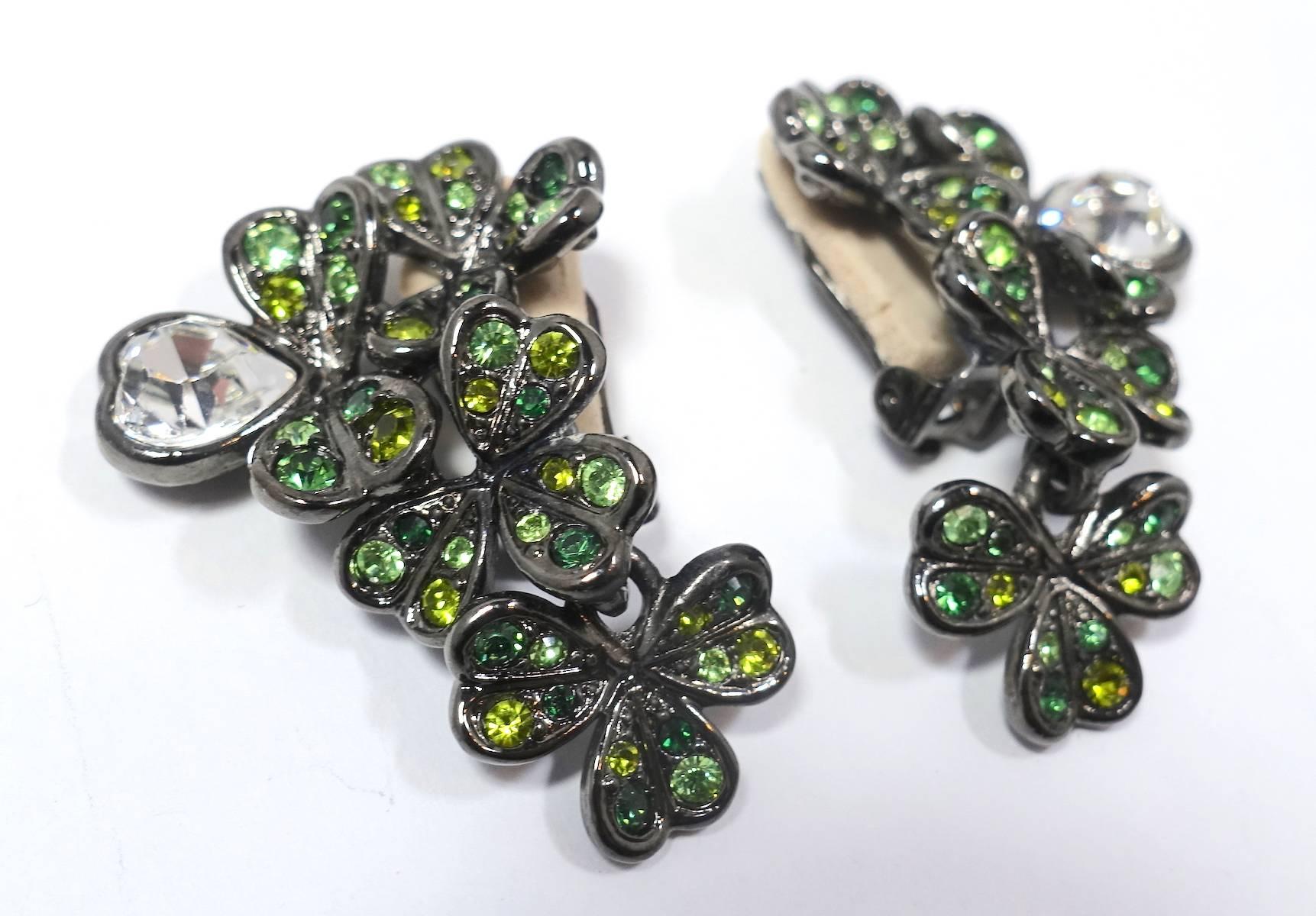 These Kenneth Jay Lane clip earrings feature a 4-leaf clover with a heart petals design. It is accented with green and clear rhinestone in a silver tone metal setting.  These earrings measure 1-1/2” x 1” and are signed “Kenneth Lane”.  They are in