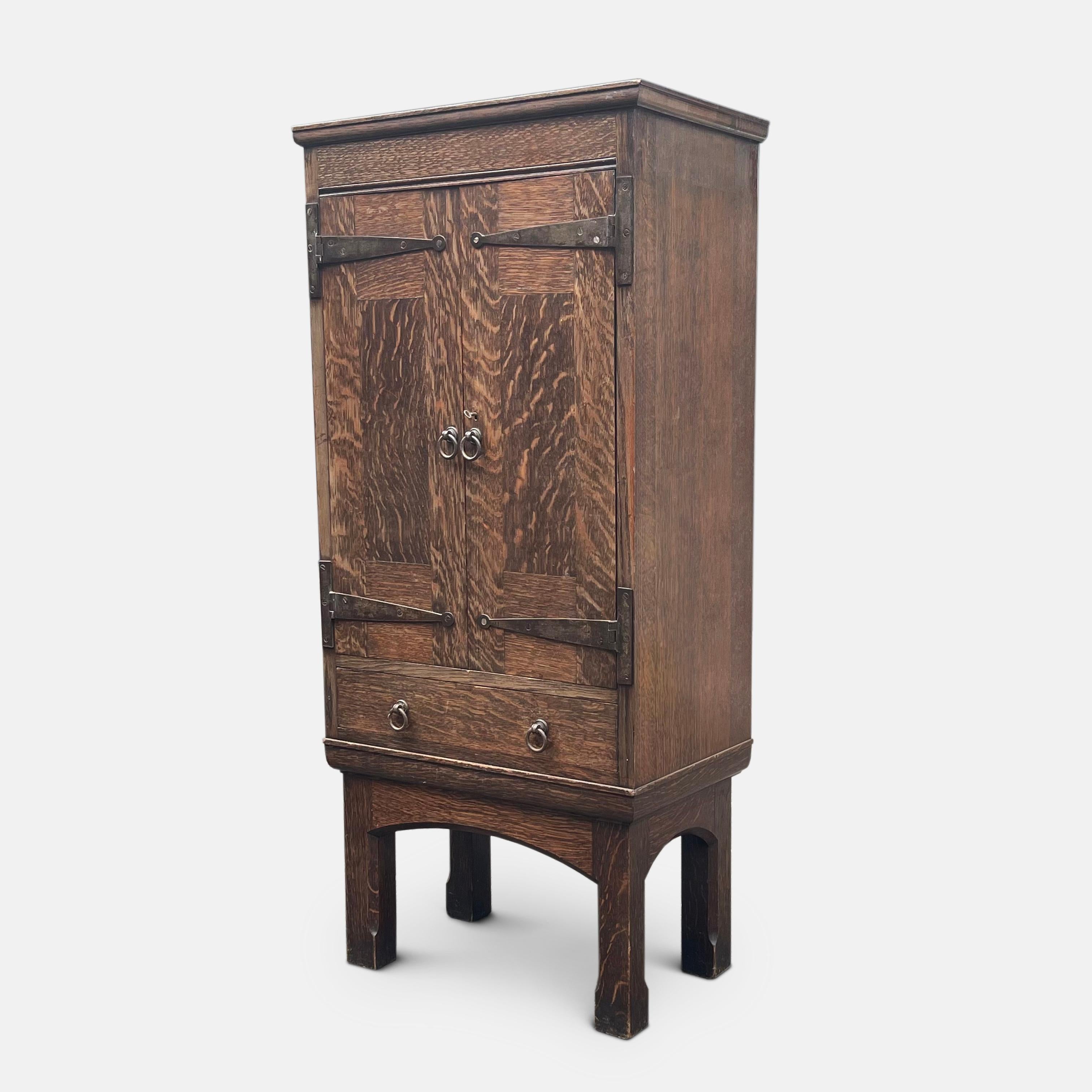 An early 20th century Liberty & Co oak cupboard attributed to Leonard Wyburd.

This piece is constructed from beautifully grained oak, enriched with hand hammered wrought iron escutcheons, circular drop handles and mounted over a frieze drawer,