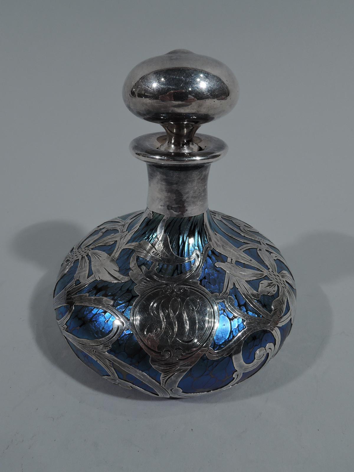 Art Nouveau iridescent glass perfume by historic maker Loetz, circa 1900. Bellied bowl and short neck with flat rim. Silver ball stopper with short clear glass plug. Glass is veined and mottled iridescent blue. Loose floral silver overlay with big