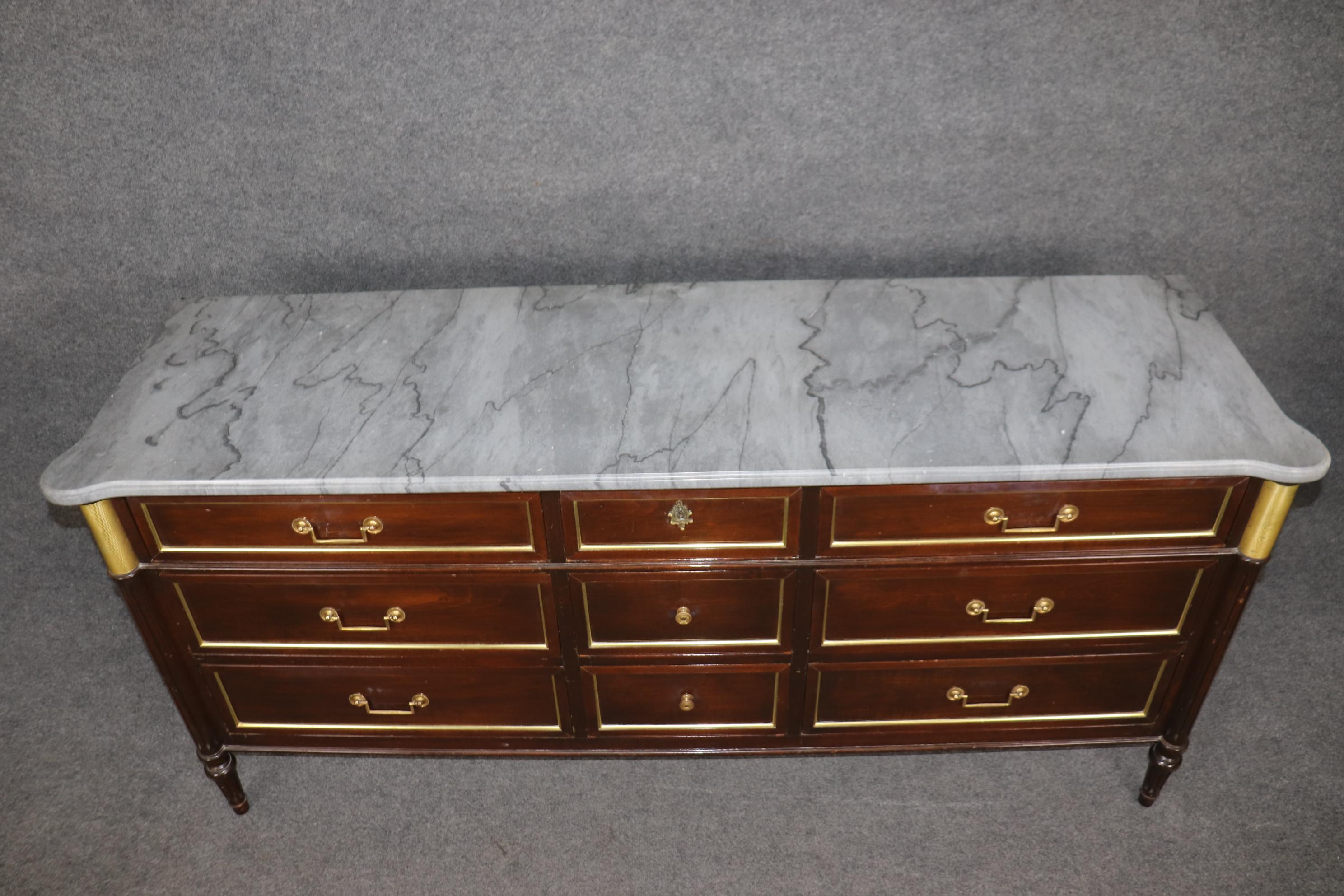 This is a superb brass trimmed gray marble top signed Maison Jansen STYLE triple dresser. The piece has wonderful bronze mounts and a gorgeous gray veined marble top. The piece is used distressed condition and can be completely detailed and