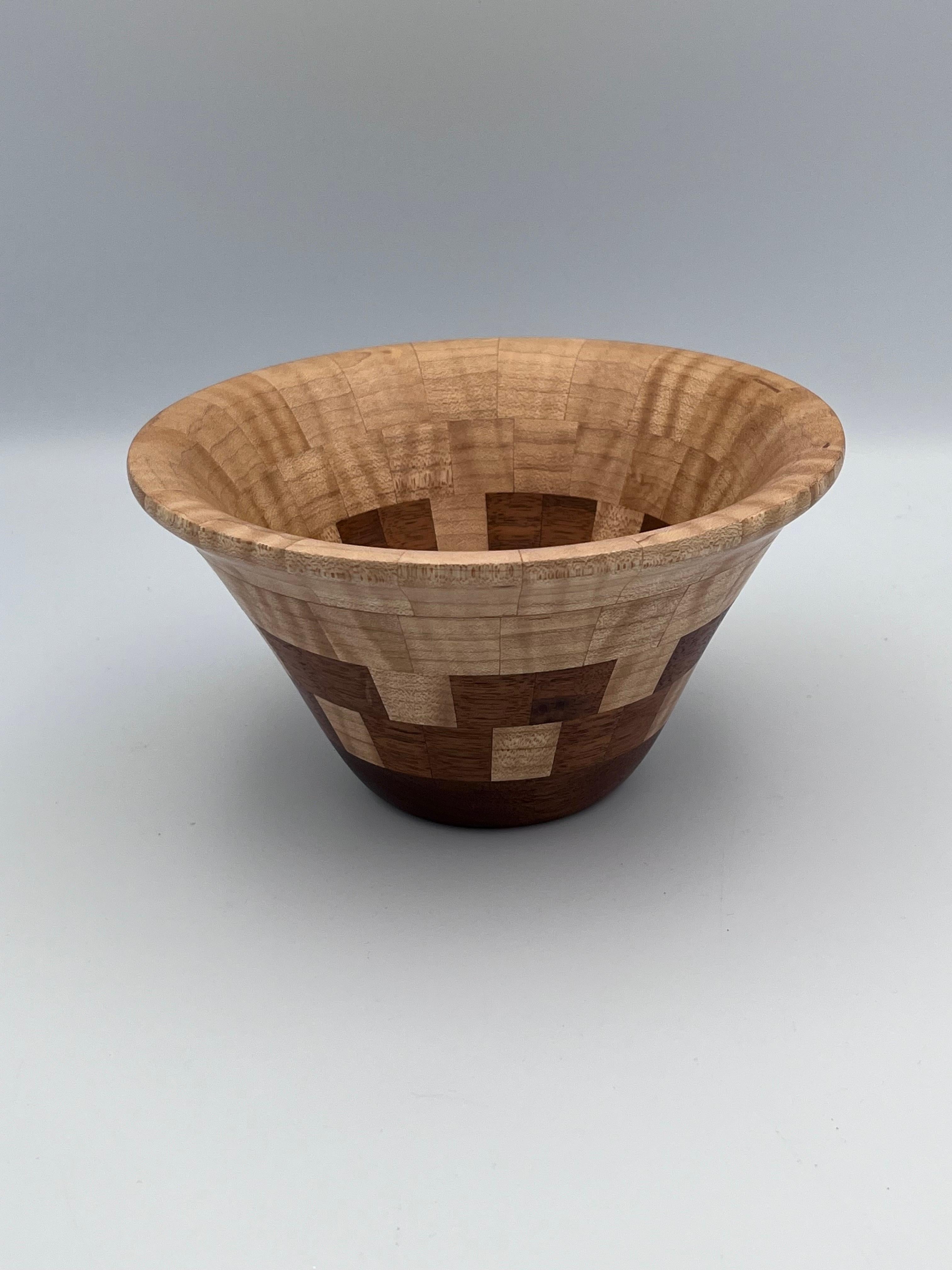 Diese wunderschöne handgefertigte Dekoschale des Kunsthandwerkers John Sinosky zeigt ein raffiniertes geometrisches Design aus warmem Ahorn- und Walnussholz. Das Stück ist auf der Unterseite signiert und weist eine charmante, gestempelte Blumenmarke
