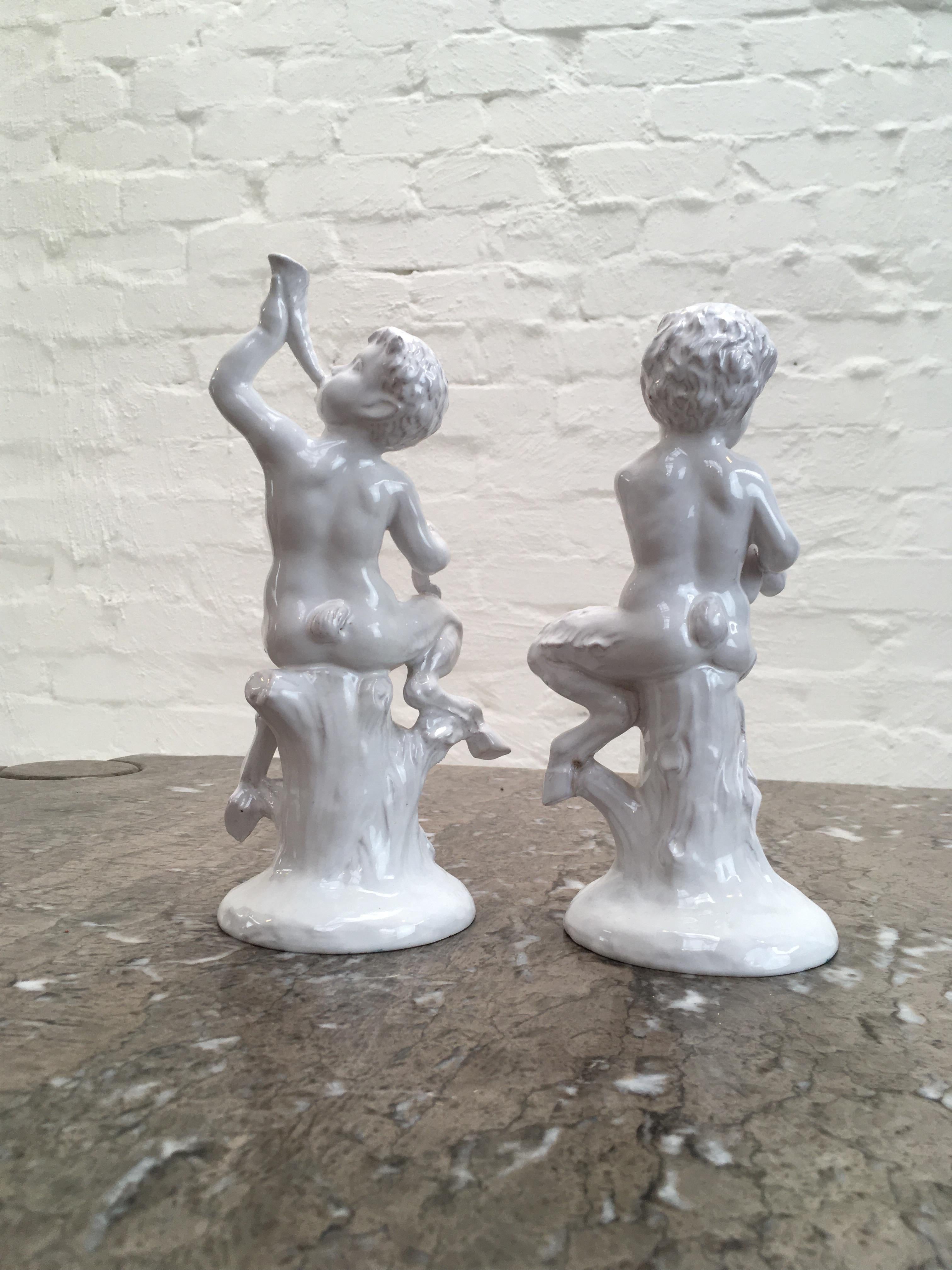 A pair of cherubic fauns, playing music. One sports a cupid's bow in one hand and blows a conch Horn. A quiver of cupid's arrows lies at his feet. The second faun accompanies on a bagpipe, his cheeks puffed and his eyes closed in concentration. They