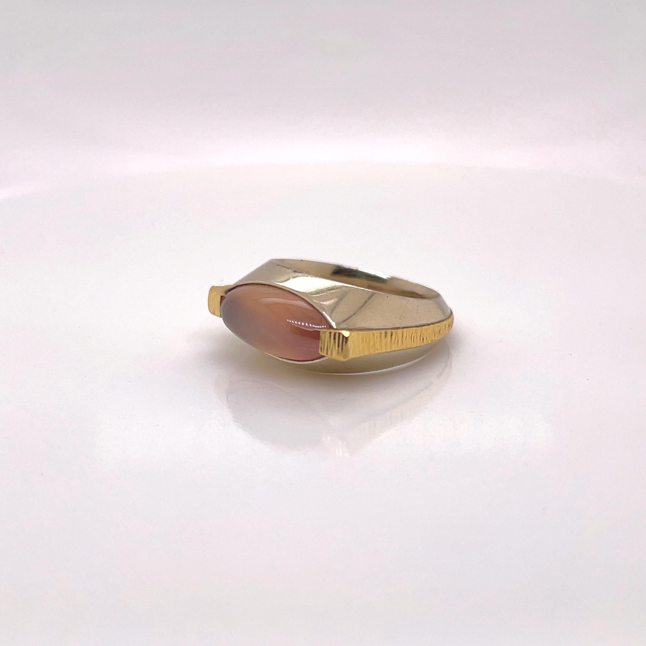 A very fine signed Modernist gold and sapphire cocktail ring.

By Cary Stefani and the Mettal Studios Inc.

In 18 karat yellow and 14 karat white golds.

Prong set with a smooth, marquee-shaped pink sapphire cabochon.

The Mettal Studios Inc. became