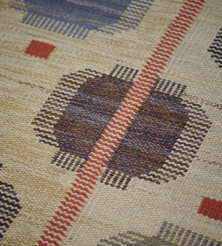 This vintage handwoven Swedish rug has an overall ivory oat field with diagonal rows of stylized graphic geometric pendants, interrupted by a delicate complementary rust stripe. Signed by the original workshop.

About the master weaver:
The