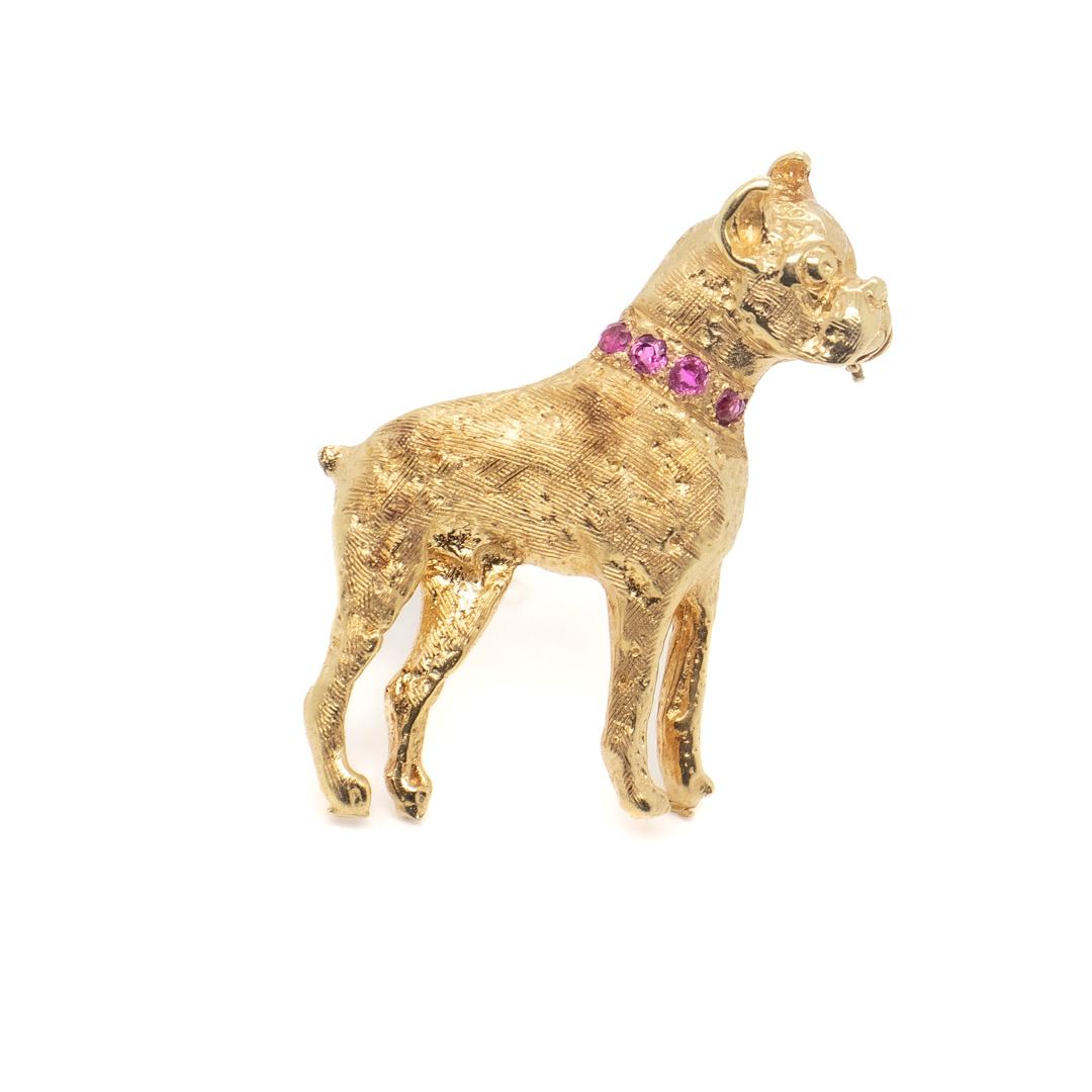A fine American Mid-Century brooch or pin.

In 14k gold.

In the form of a boxer dog standing erect and alert with a ruby studded collar around its neck and with a brushed finish throughout.

Marked for the Henry S Bick Company of New York,