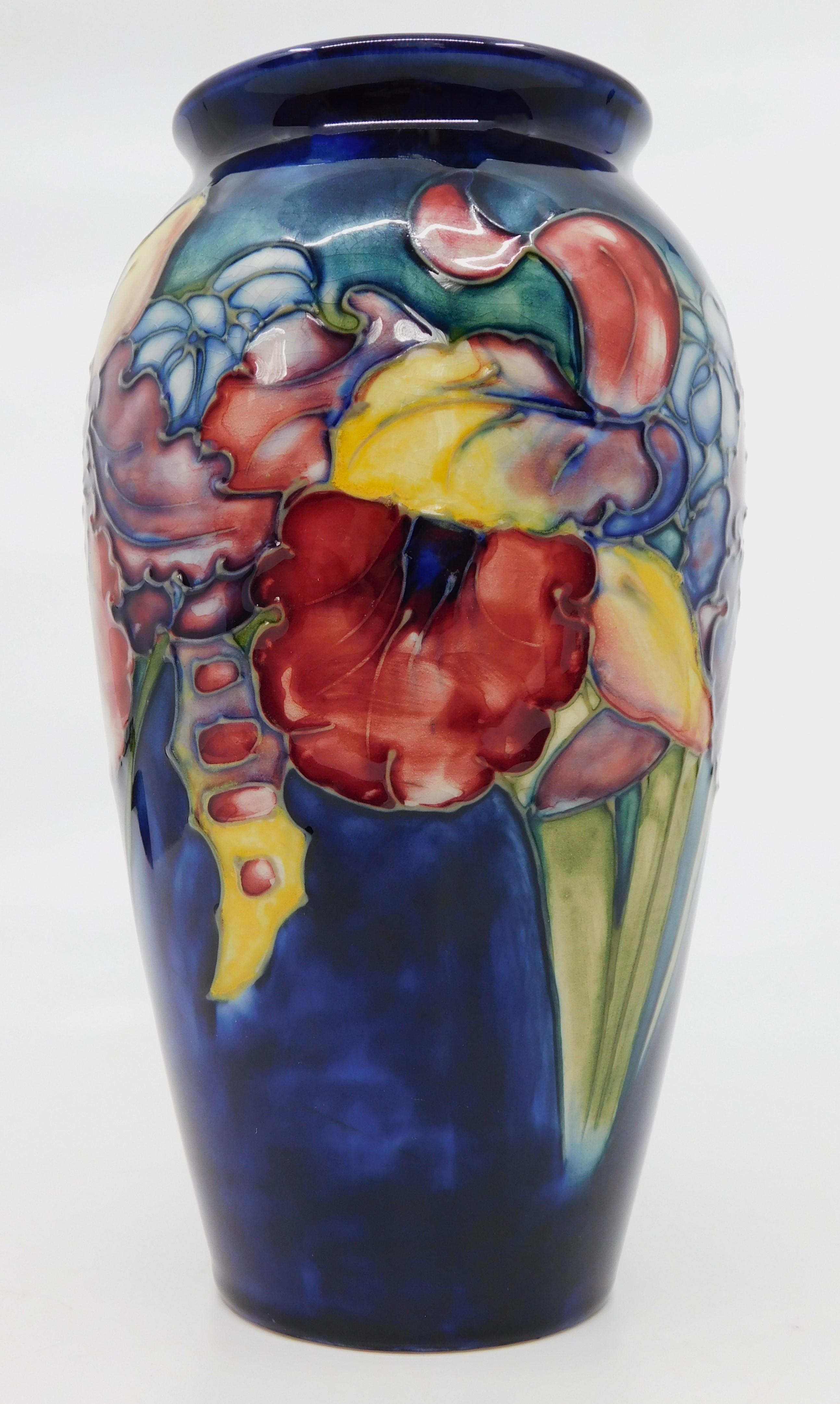 This signed art pottery vase was done by the Moorcroft Pottery company of England in circa 1950 using their signature deep cobalt blue ground and done in the 'Hibiscus' flower pattern.  Designed and produced by William Moorcroft It features fine