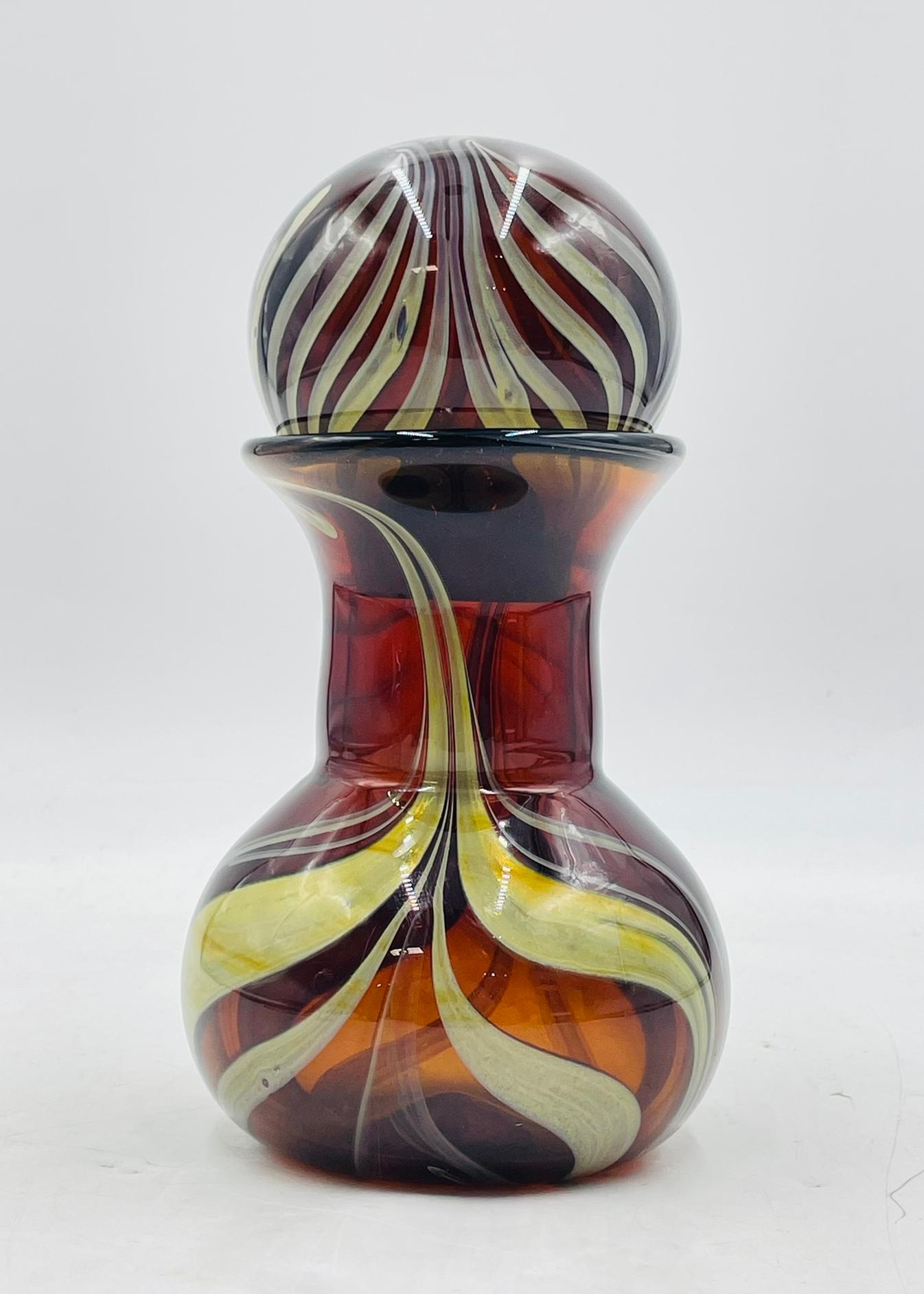 This vibrant Murano art glass jar with lid is a signed and dated work by C. Rachke, created in 1992. Hand-blown in Italy, the piece features a rich amber body with dynamic swirling ribbon patterns in cream, yellow, and pale green. The matching