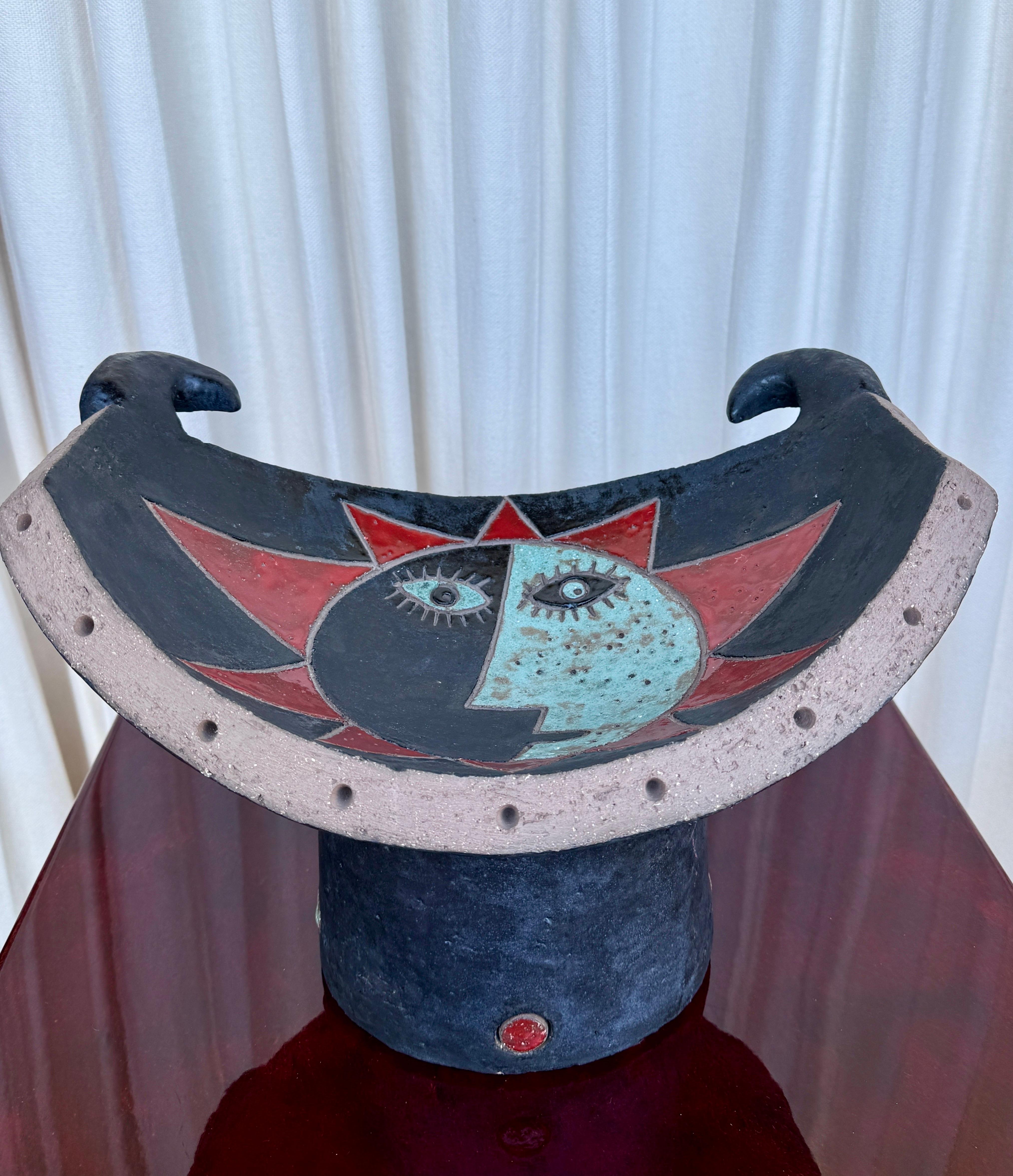 Voici un magnifique centre de table en céramique de Nathalie Soufflet, France.  Imagerie très Picasso, comme la double face solaire et les cornes de taureau, finition en glaçure mate noirâtre/bleu et rouge.  Signé au verso, de sa série 
