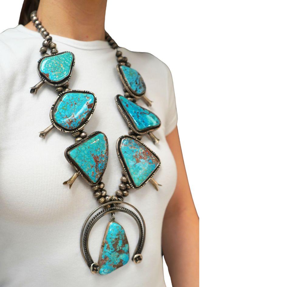 This is a Navajo squash blossom necklace handcrafted in sterling silver and turquoise, signed NB, a hallmark attributed to Nellie B. Nez, a Native American silversmith known for traditional Navajo jewelry. The necklace features a bold naja pendant,
