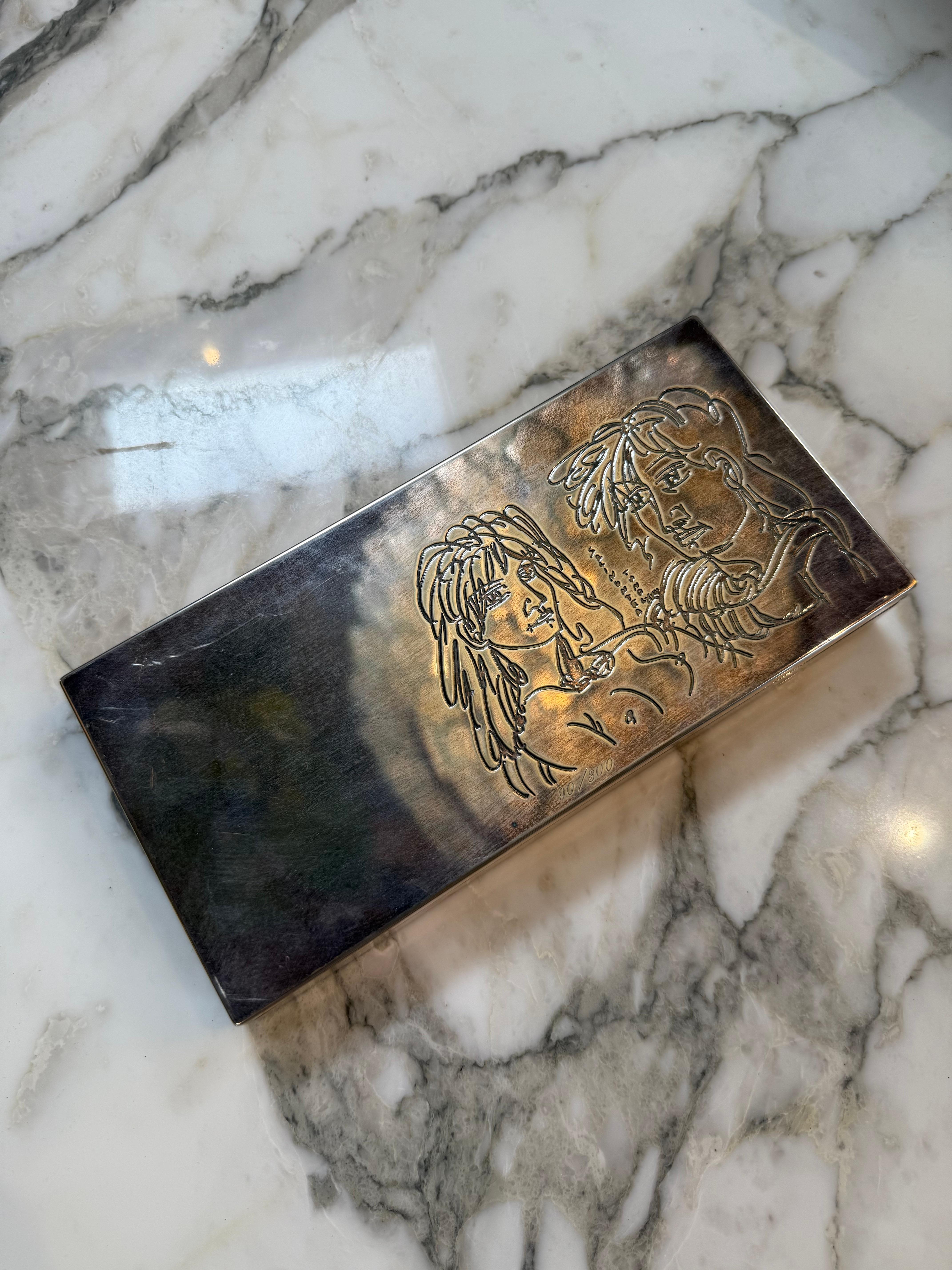 An exquisite silver-plated decorative box designed by Cleto Munari, featuring a finely engraved dual portrait on its lid. The artwork showcases two expressive faces drawn in Munari’s distinctive minimalist, modernist line style, evoking a sense of