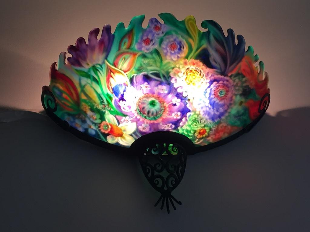 Signed original Ulla Darni sconce is reverse painted on glass with hand-forged iron work. The top is hand-carved. Ulla starts with a blank glass surface to paint on. She uses vibrant colors that pop off the glass, making it feel like the sconce is