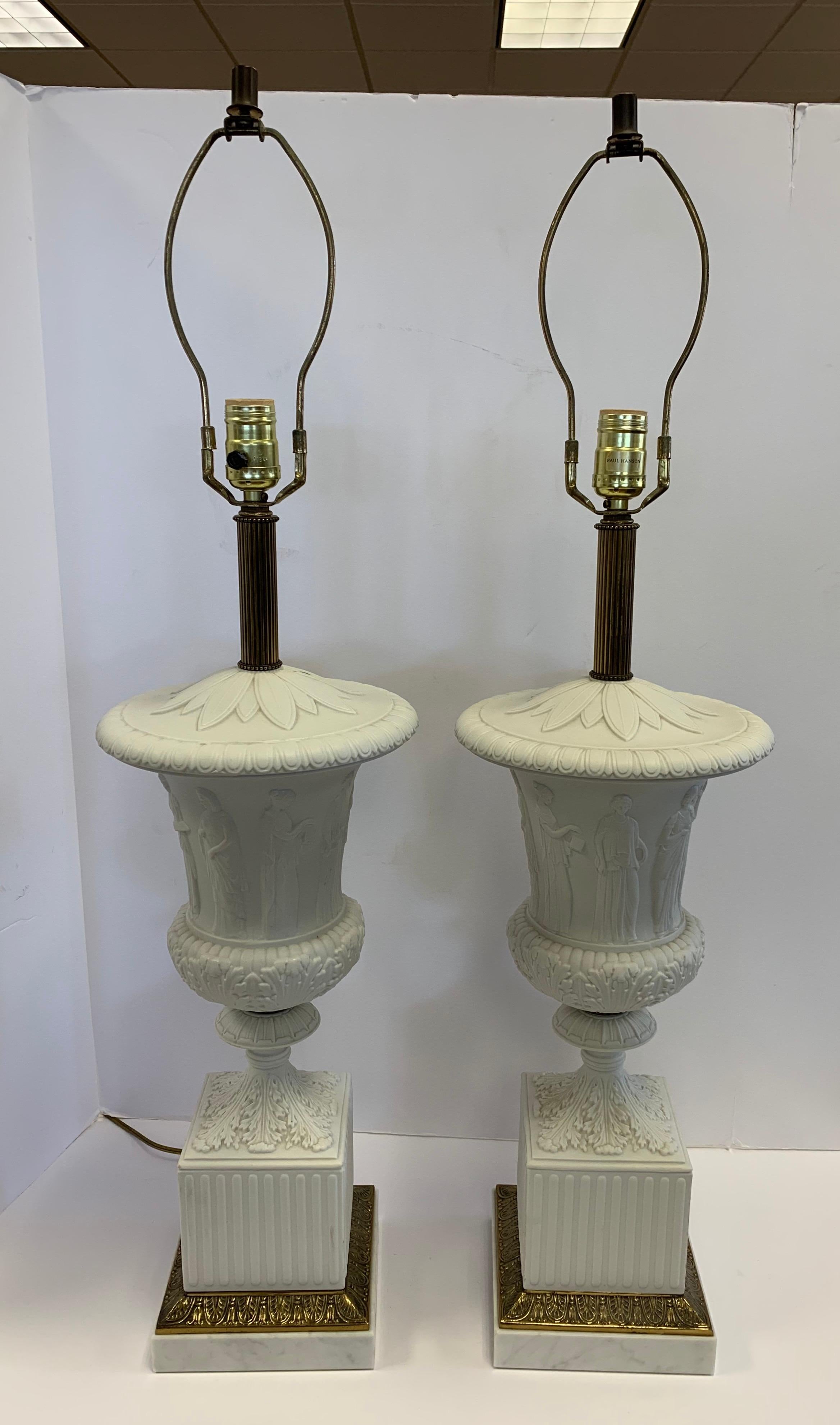 Stunning pair of neoclassical Paul Hanson white urn form porcelain table lamps with carrara  marble bases. Feature a raised design of classical female figures all and acanthus leaf detail all around. Luxurious color, scale and design. All hallmarks