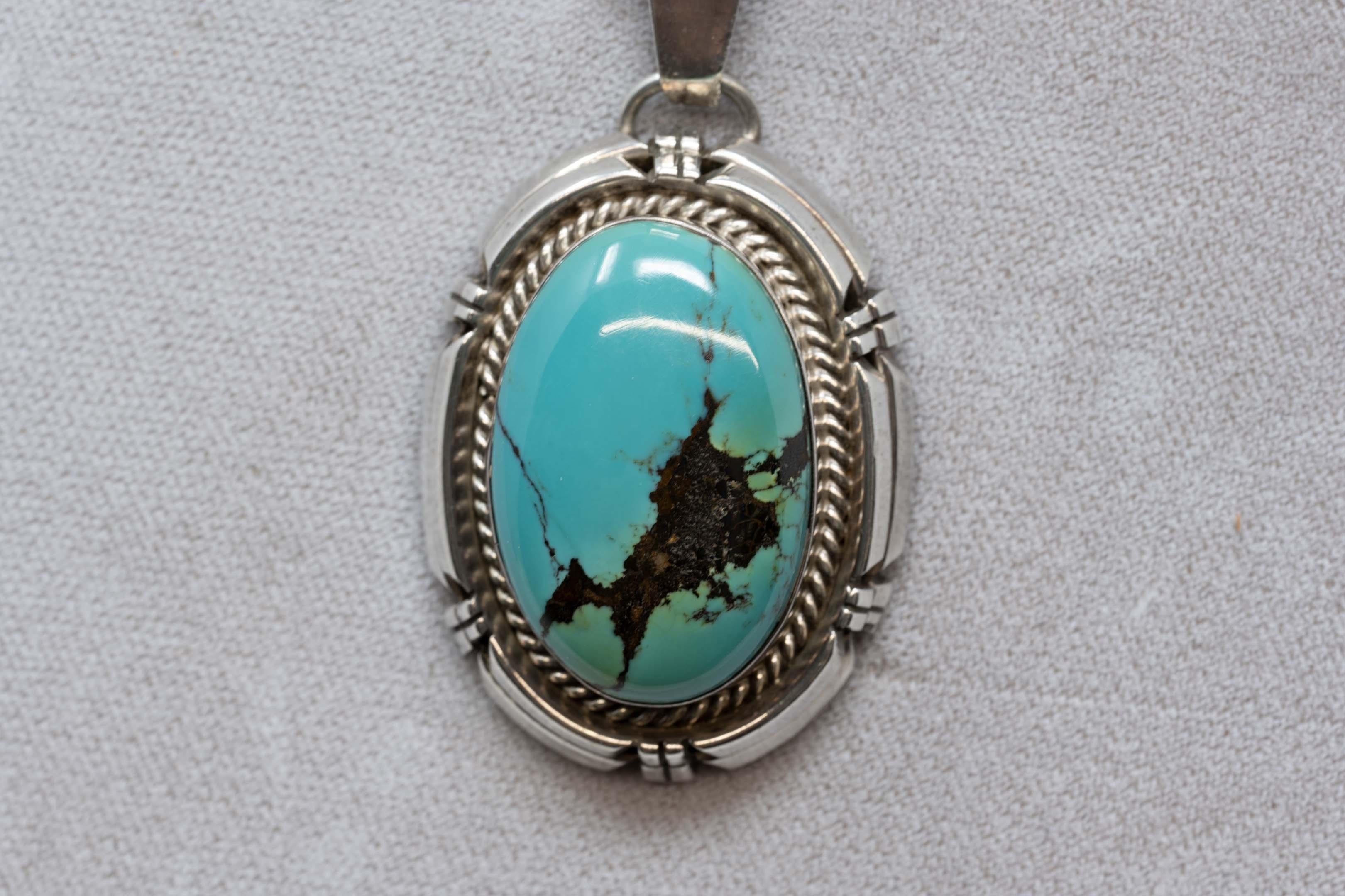 Pendentif en argent turquoise signé et réalisé par Rita Touchine, orfèvre Navajo. La pierre mesure 32 x 22 mm, le pendentif mesure 45 x 33 mm sans le loup. Fabriqué aux États-Unis à la fin du XXe siècle.