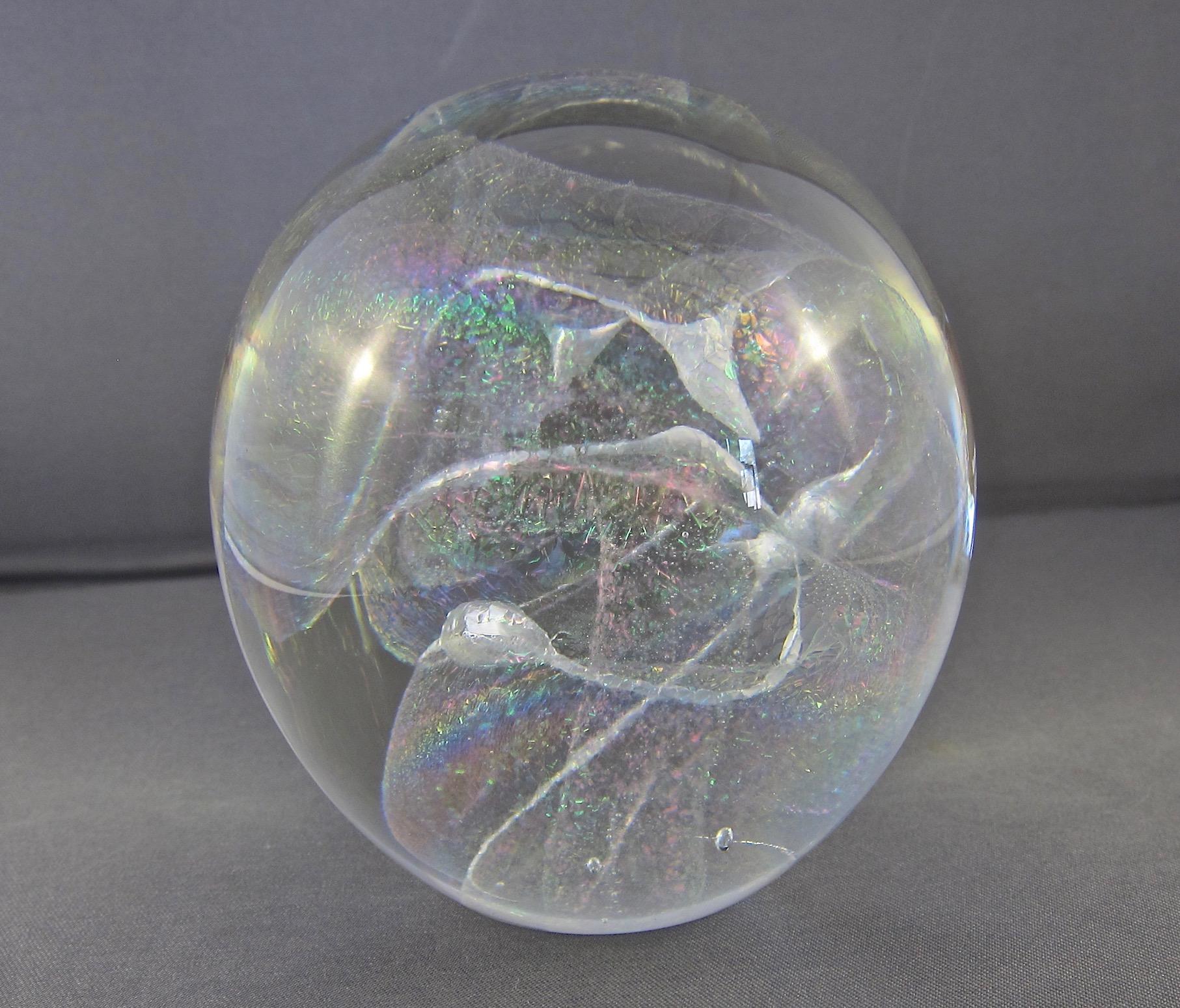 A signed vintage art glass paperweight by American glass artist, Robert W. Stephan dating to 1987. This clear glass sphere was handcrafted with colorful internal iridescence and swirls, creating sparkling color shifts that transform the design when