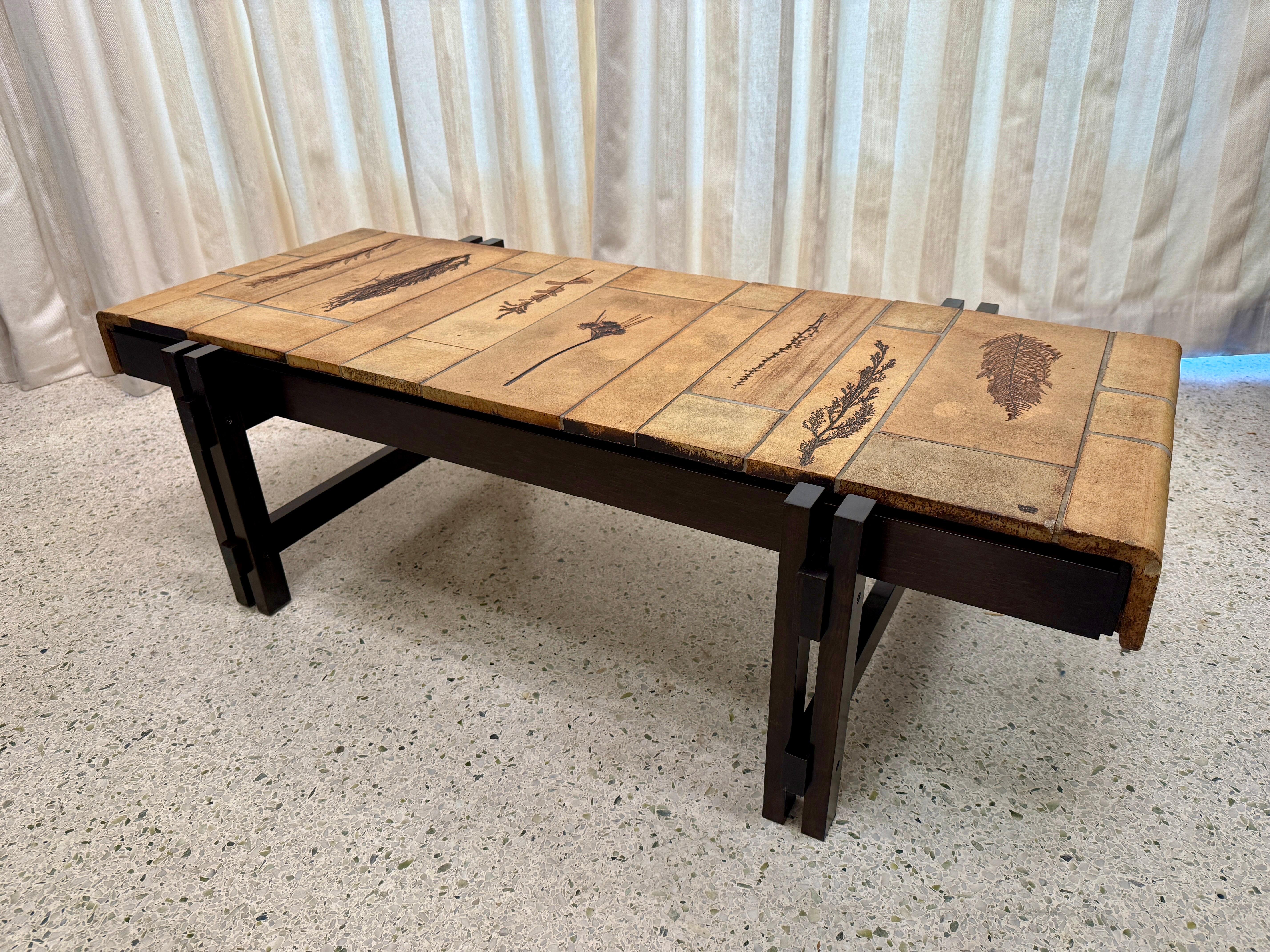 Table basse aux tons naturels et terreux, conçue par le céramiste français Roger Capron au milieu du 20e siècle.  Il se compose d'une base en bois richement colorée et d'un magnifique plateau en céramique de style cascade avec des fleurs imprimées