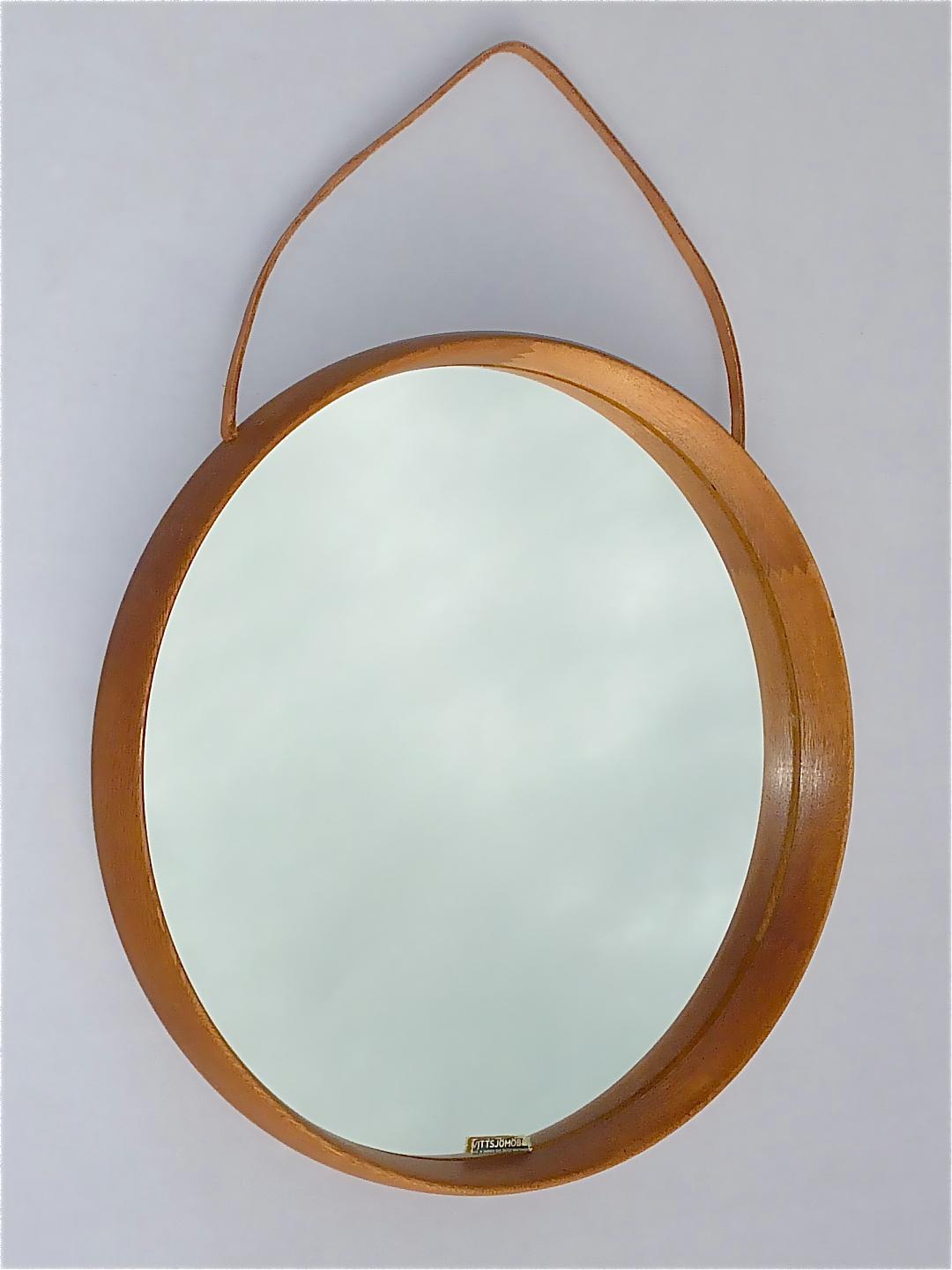 Signed round Swedish brown oak wood wall mirror with leather strap designed by renowned Uno & Östen Kristiansson and produced by Vittsjö möbel in Sweden circa 1960s. The handmade Scandinavian modern mirror of high quality which has a width of 45 cm