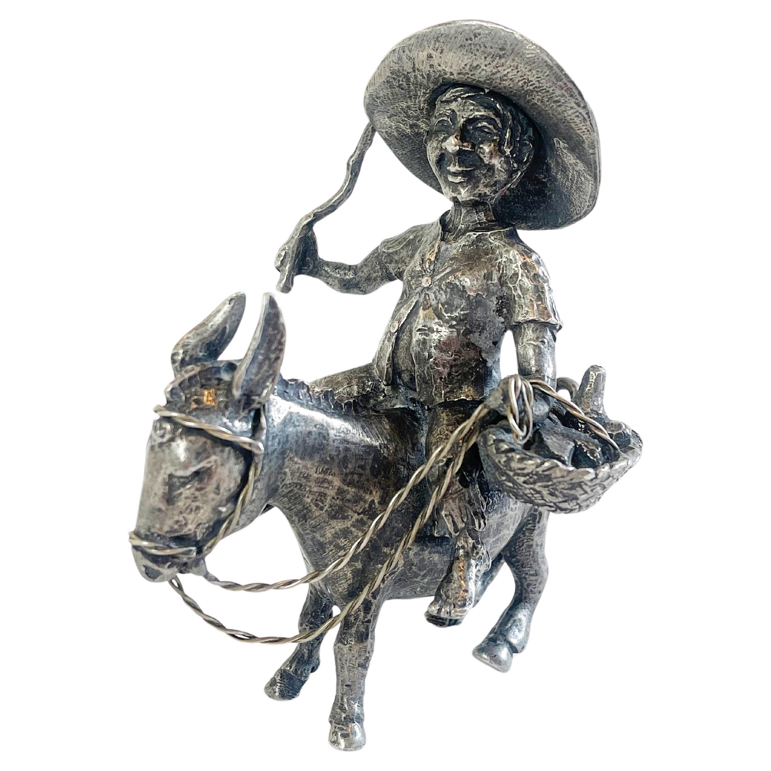 Figurine of the character of Sancho Panza, who was Don Quixotes companion. 
Here he is riding is donkey, carrying a basket with cheese, a bottle of wine and sorts over his left arm, a stick in his
left hand. His oversized Mexican style hat provides