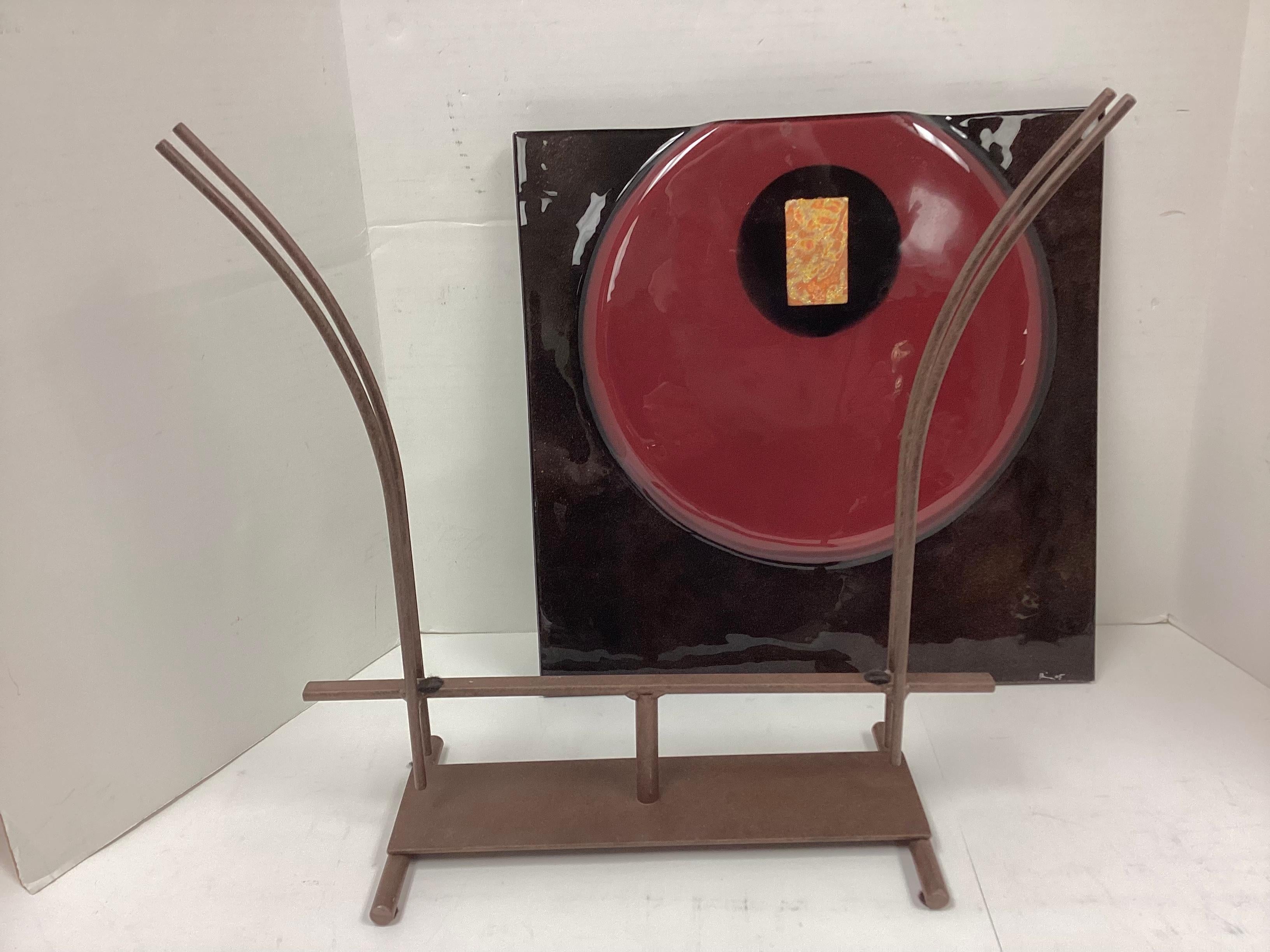 Un grand vase en verre d'art signé, décoratif et coloré, en verre rouge et noir, monté sur un support en fer de style industriel. Le vase à motif géométrique du cercle rouge à l'intérieur  le carré de verre noir.  Un cercle noir intérieur contient