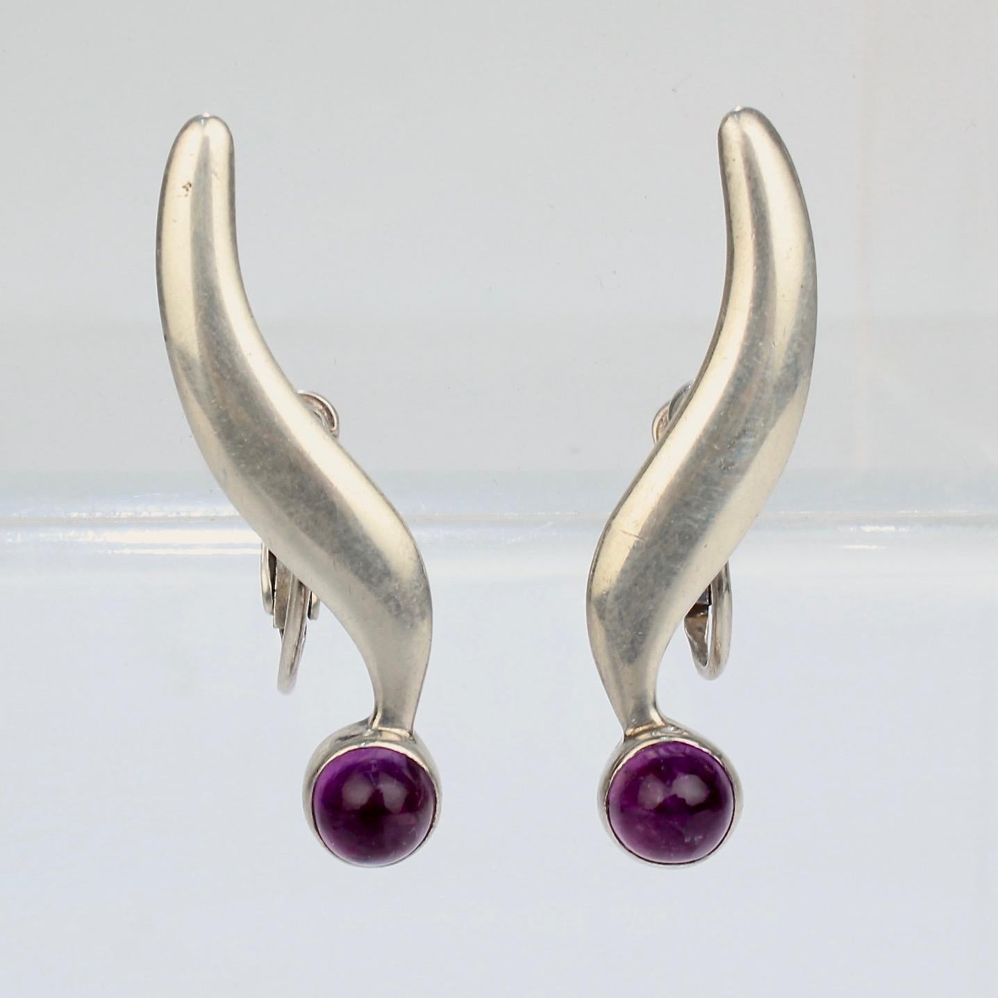 A fine pair of vintage Modernist Mexican screw back earrings.

Signed Sigi.

In sterling silver earrings with smooth round amethyst cabochons. 

Marked on reverse: STERLING and Mexico, HECHO, SIGI, TASCO and 810.

Date:
Mid-20th Century

Overall