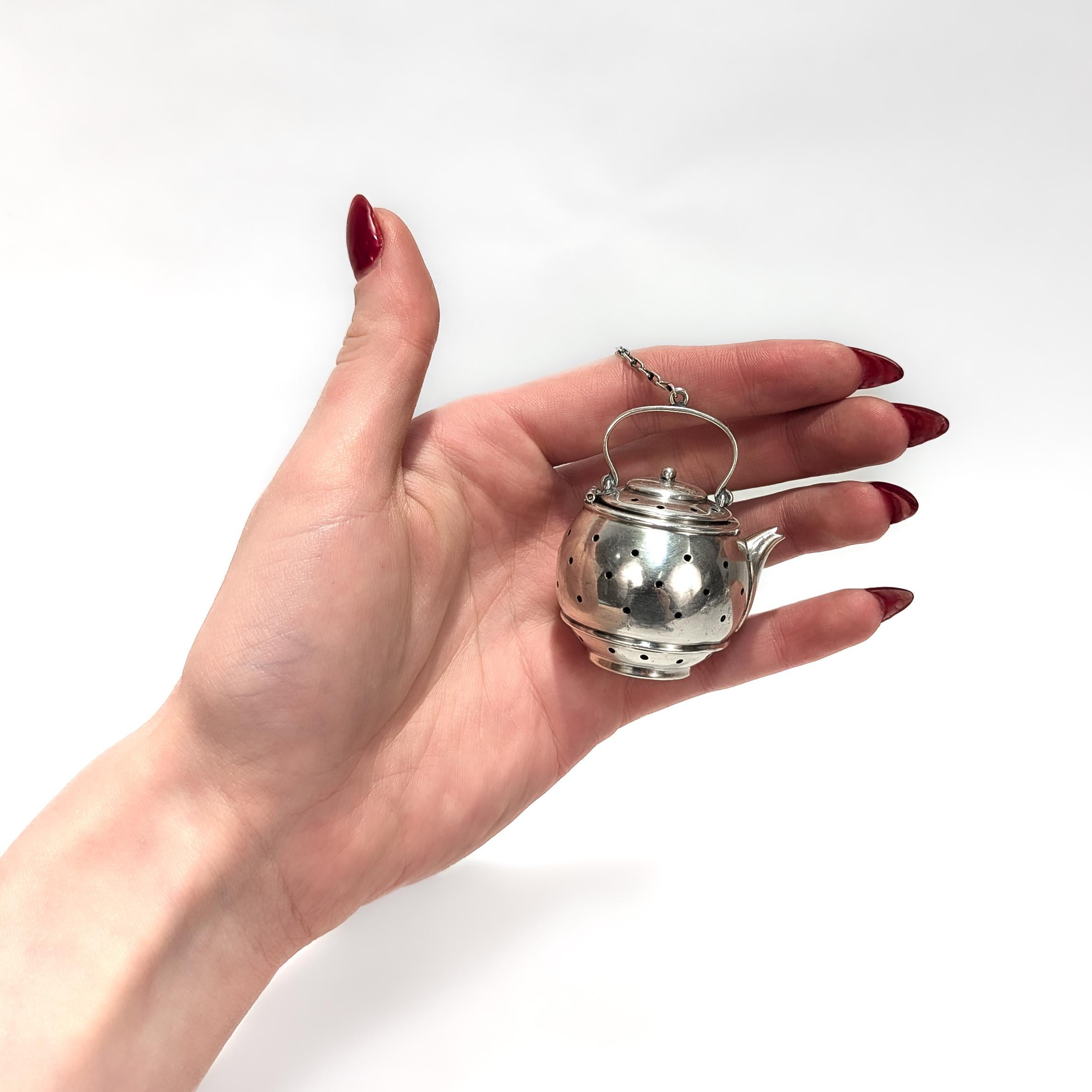 A fine figural tea strainer.

In sterling silver.

By Simons Bros. of Philadelphia, PA.

In the form of a teapot with a chain & spout ring attached to the top handle.

Fully marked to the base.

Simply a wonderful antique tea strainer!

Date:
Early