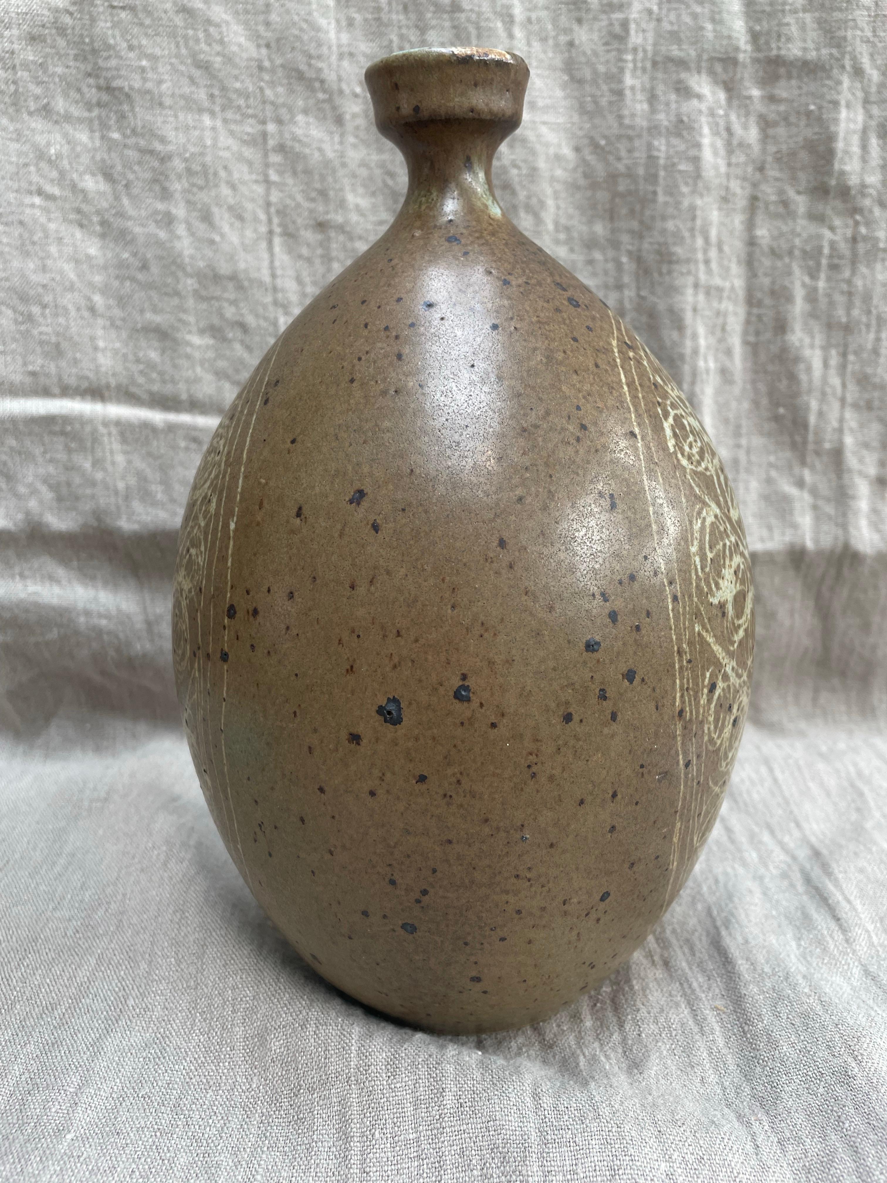 Un étonnant vase en poterie Studio du milieu du 20e siècle, tourné à la main avec un corps arrondi et un col étroit, fini dans une glaçure terreuse chaude. La surface est décorée d'un sgraffite incisé représentant un arbre stylisé ou une forme de