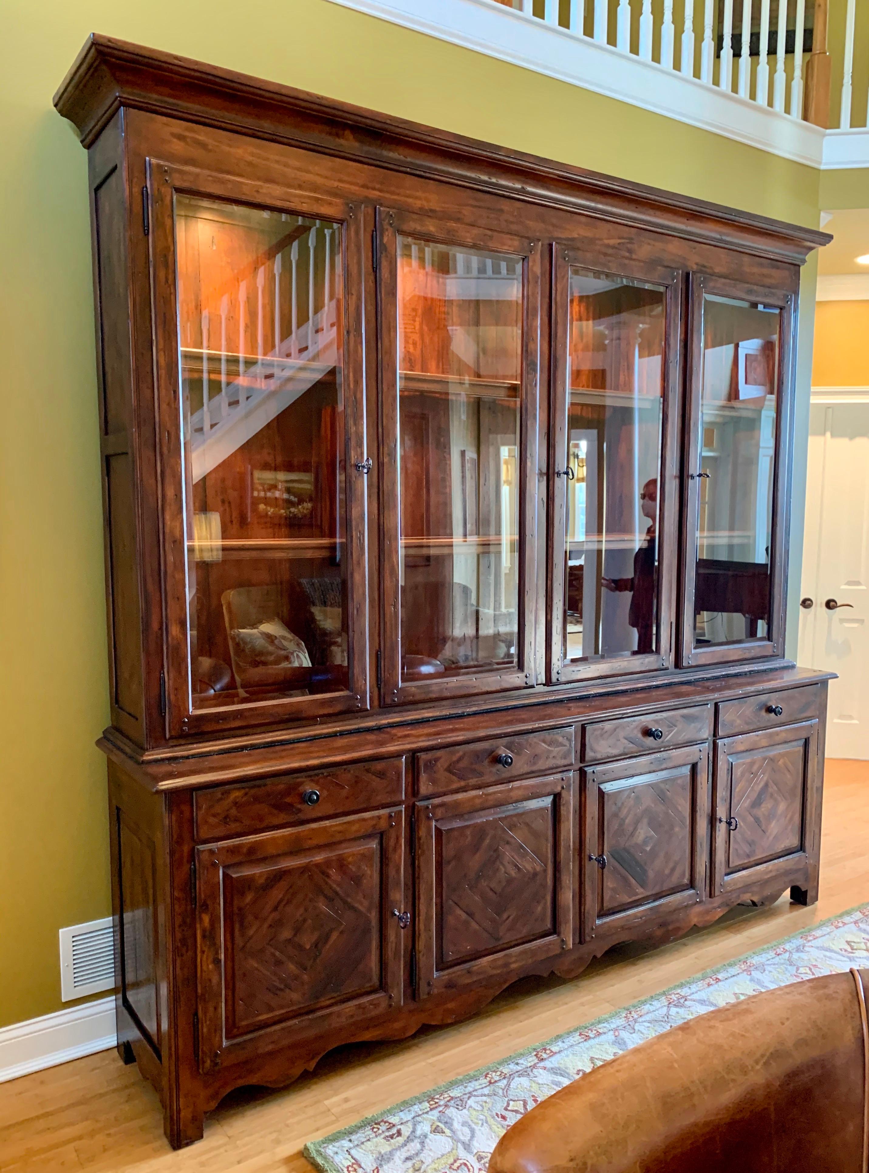 Theodore Alexander Castle Bromwich large china display cabinet has an antique mahogany finish and antique brass hardware. Top part has four glass doors and is illuminated from above unto its adjustable glass shelves. Bottom portion has four drawers