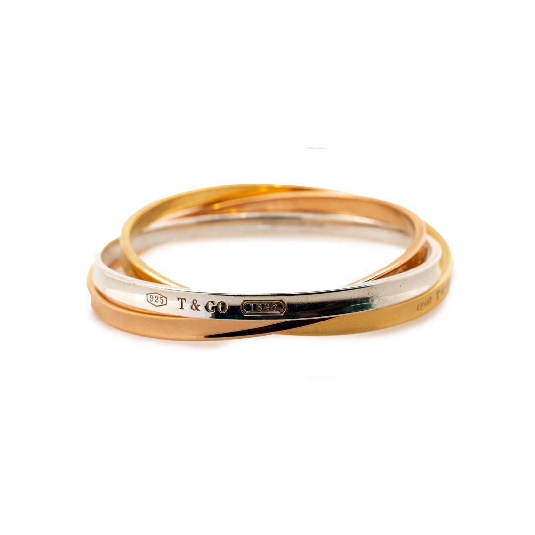 One lady's designer made polished, 18K tri-color gold and silver, bangle bracelet. The bracelet measures approximately 7.50 inches in length by 5.00mm in diameter each bangle and weighs a total of 77.87 grams. Engraved with 