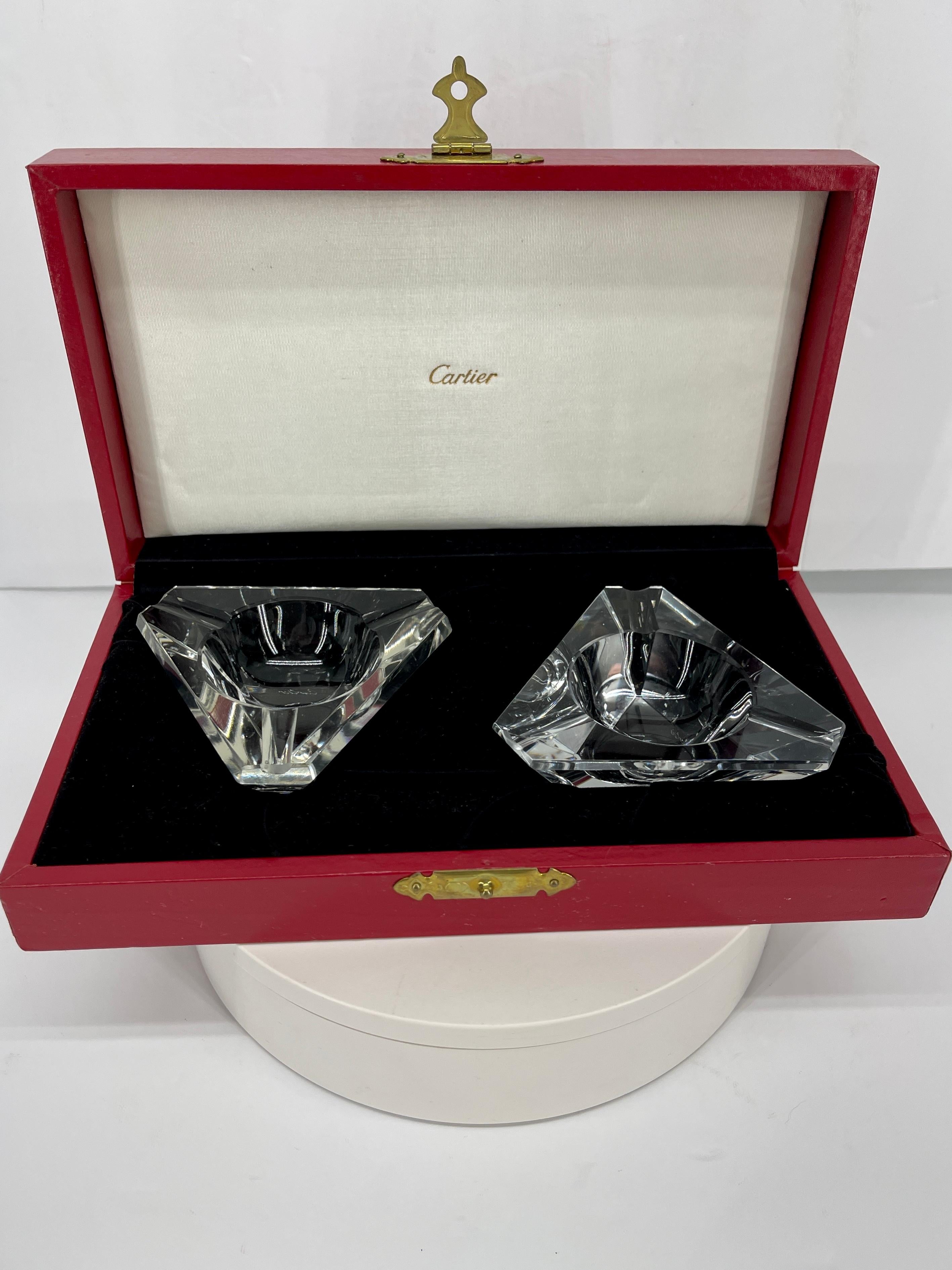 Set of Cartier faceted crystal ashtrays. This beautiful pair of ashtrays is nestled in the original red leather Cartier box with brass accented handle. Each ashtray is signed Cartier on the bottom. The timeless set of personal ashtrays is an elegant