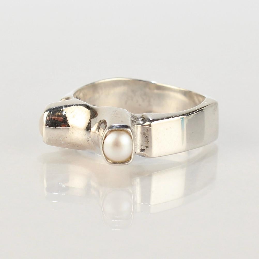 A fine, signed, modernist ring by Wesley Emmons.

Comprised of sterling silver, this modernist ring is bezel set with 2 small white pearls.

Emmons was an important jewelry maker in Philadelphia during the Mid-20th century.

He created cutting-edge