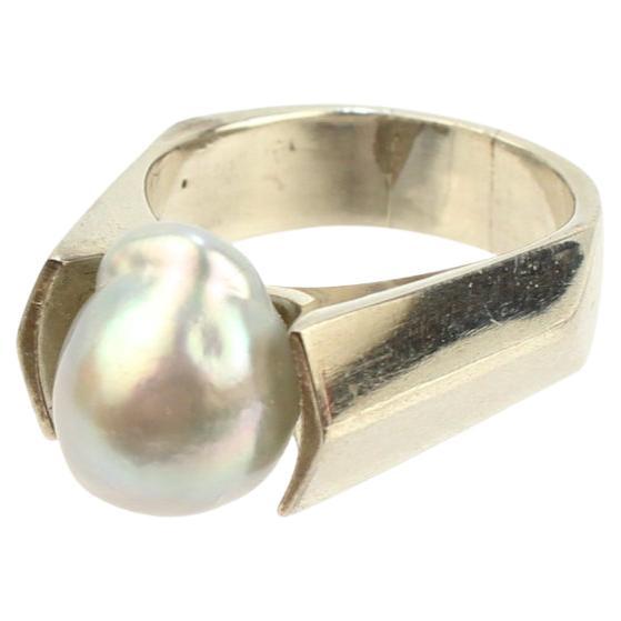 Ein beeindruckender signierter Ring von Wesley Emmons.

Dieser feine Ring mit abgeschrägtem Schaft besteht aus Sterlingsilber und ist mit einer großen grauen Barockperle besetzt.

Emmons war in der Mitte des 20. Jahrhunderts ein wichtiger