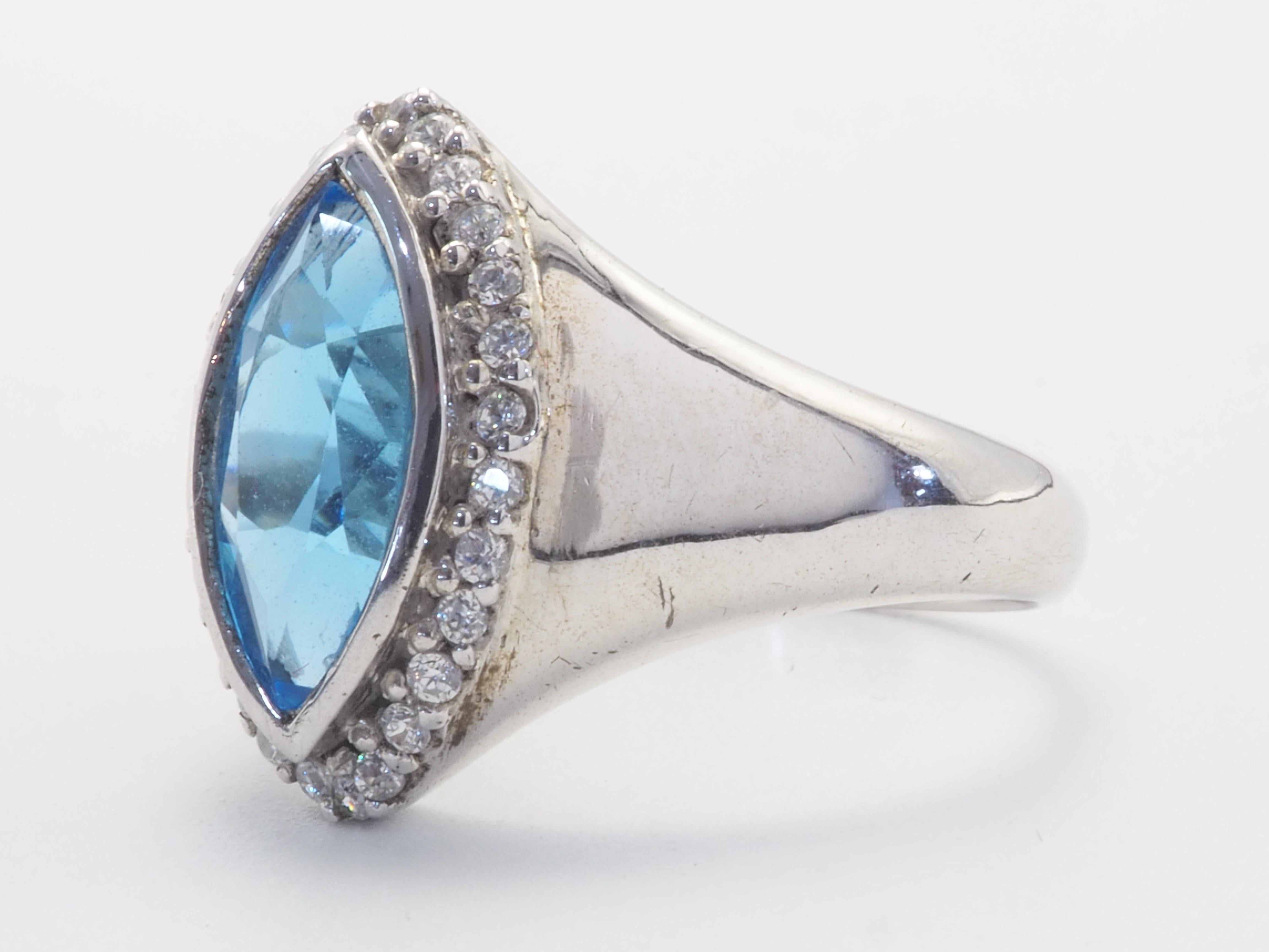 Dieser Ring ist ein Statement-Siegelring aus massivem Sterlingsilber. Der Ring ist mit einem natürlichen und stark gesättigten marquisefarbenen Schweizer Blautopas in der Mitte der Lünette verziert. Die umliegenden weißen Steine sind Quarz. Das Band