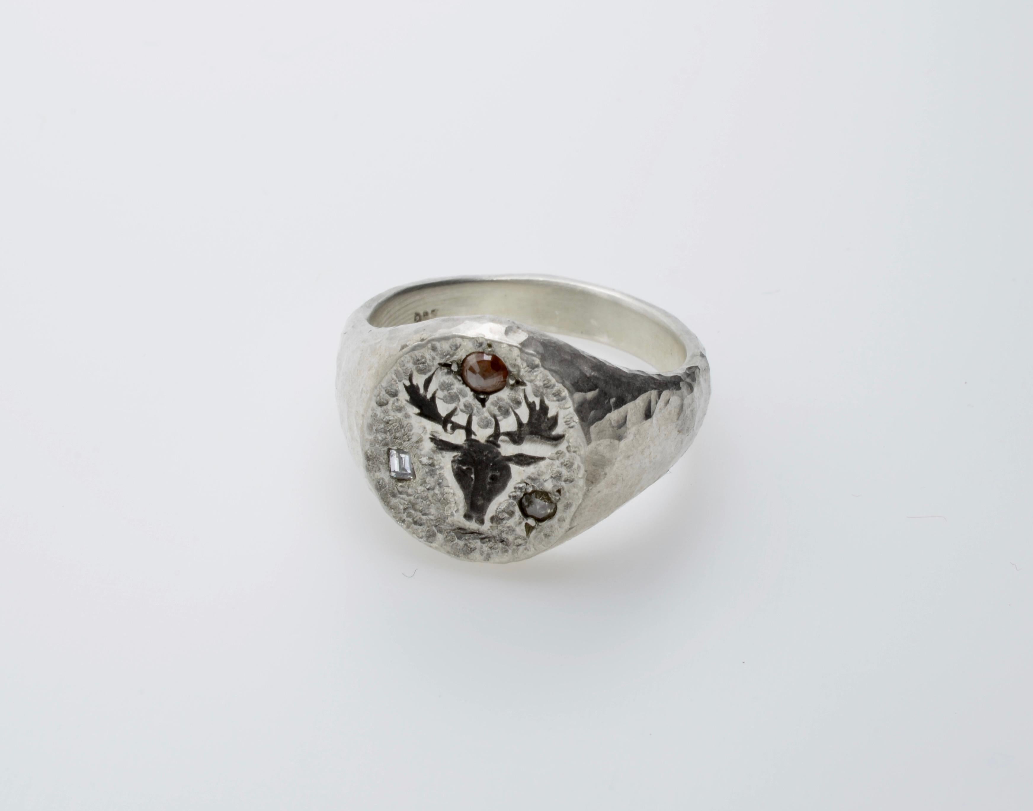 Traditional shape of a signet ring, with the particularity of the hammered texture in silver and set with diamonds. The one baguette diamond and two round diamonds are 0.15 carats total weight.  The diamonds add a modern look to the ring. The top is