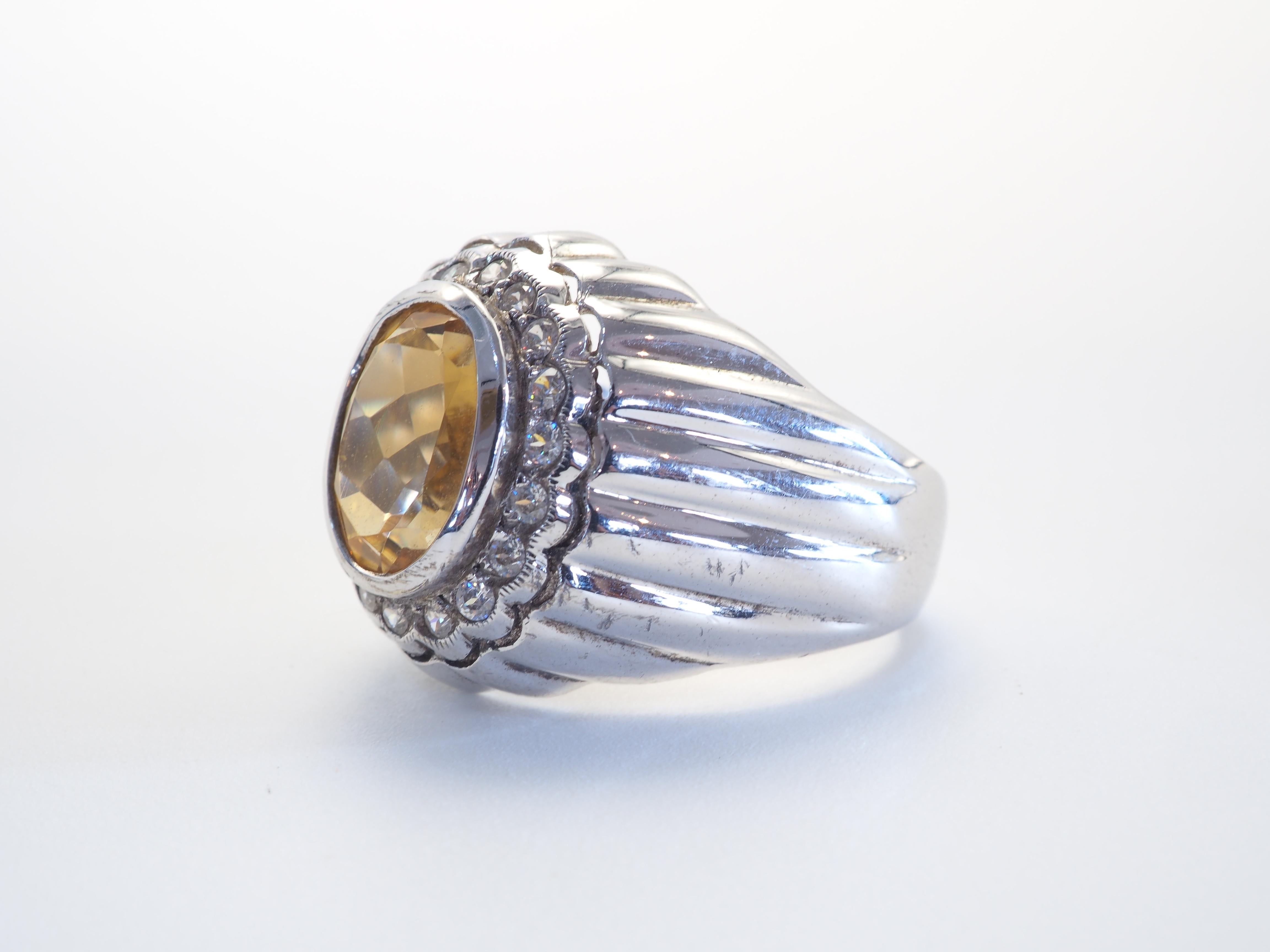 This ring is a statement signet Trombino ring in solid sterling silver. The ring is decorated by natural oval citrine bezel set in the middle. The surrounding white stones are quartz. The engraving pattern on the band is delicately carved and is