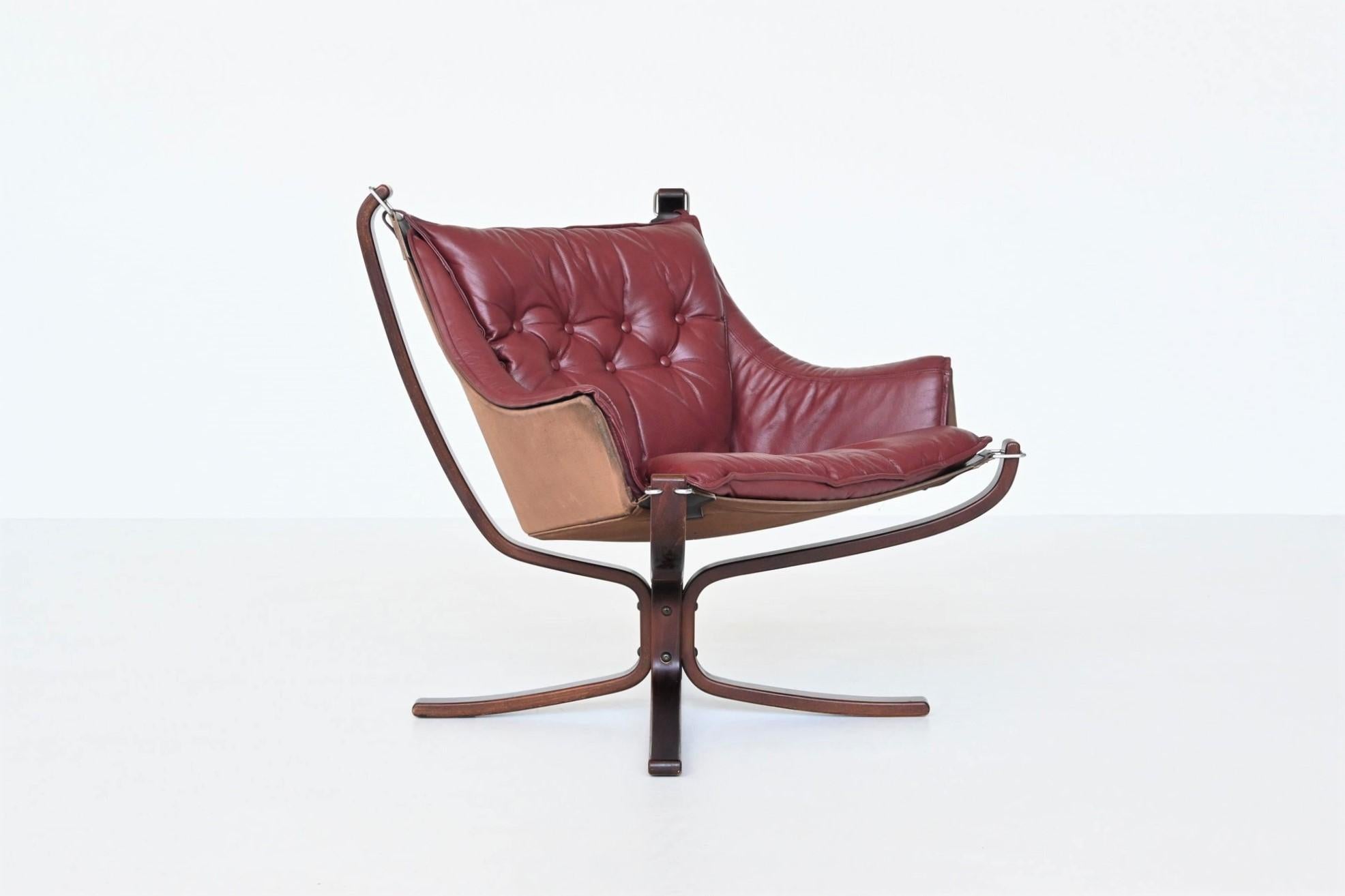 Iconic X-framed low back Falcon lounge chair designed by Sigurd Ressell for Vatne Mobler, Norway 1970. They feature a curved stained beech wooden frame, canvas sling and burgundy (red) leather cushions. The hammock style floating seat has become a