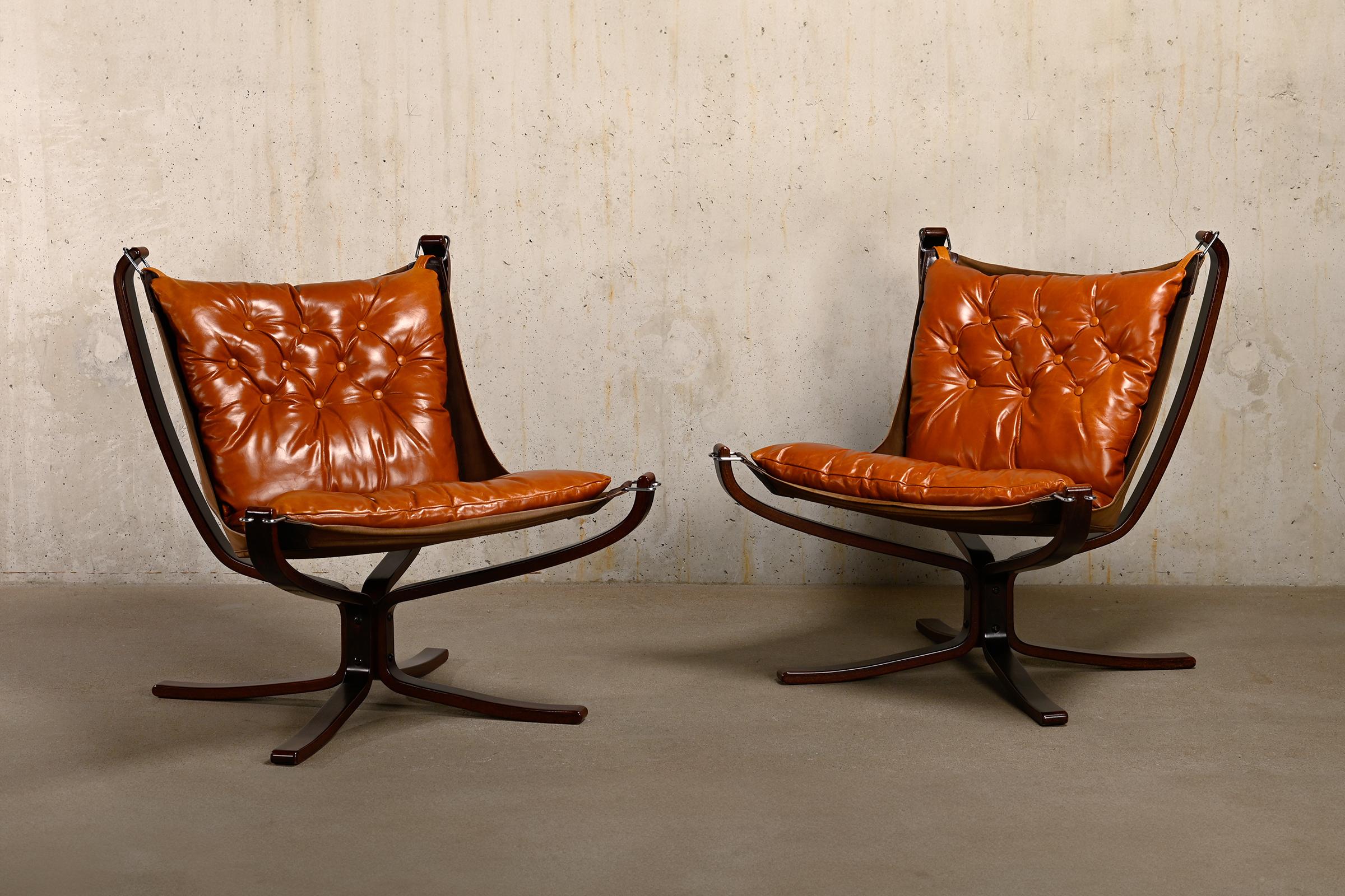 Very nice pair of 'Falcon' Lounge Chairs designed by Sigurd Ressell for Vatne Møbler, Norway 1970's. Curved dark brown stained wooden frame connected by a metal plate. Hanging in it is a canvas seat with cognac-colored leather cushions. Very good